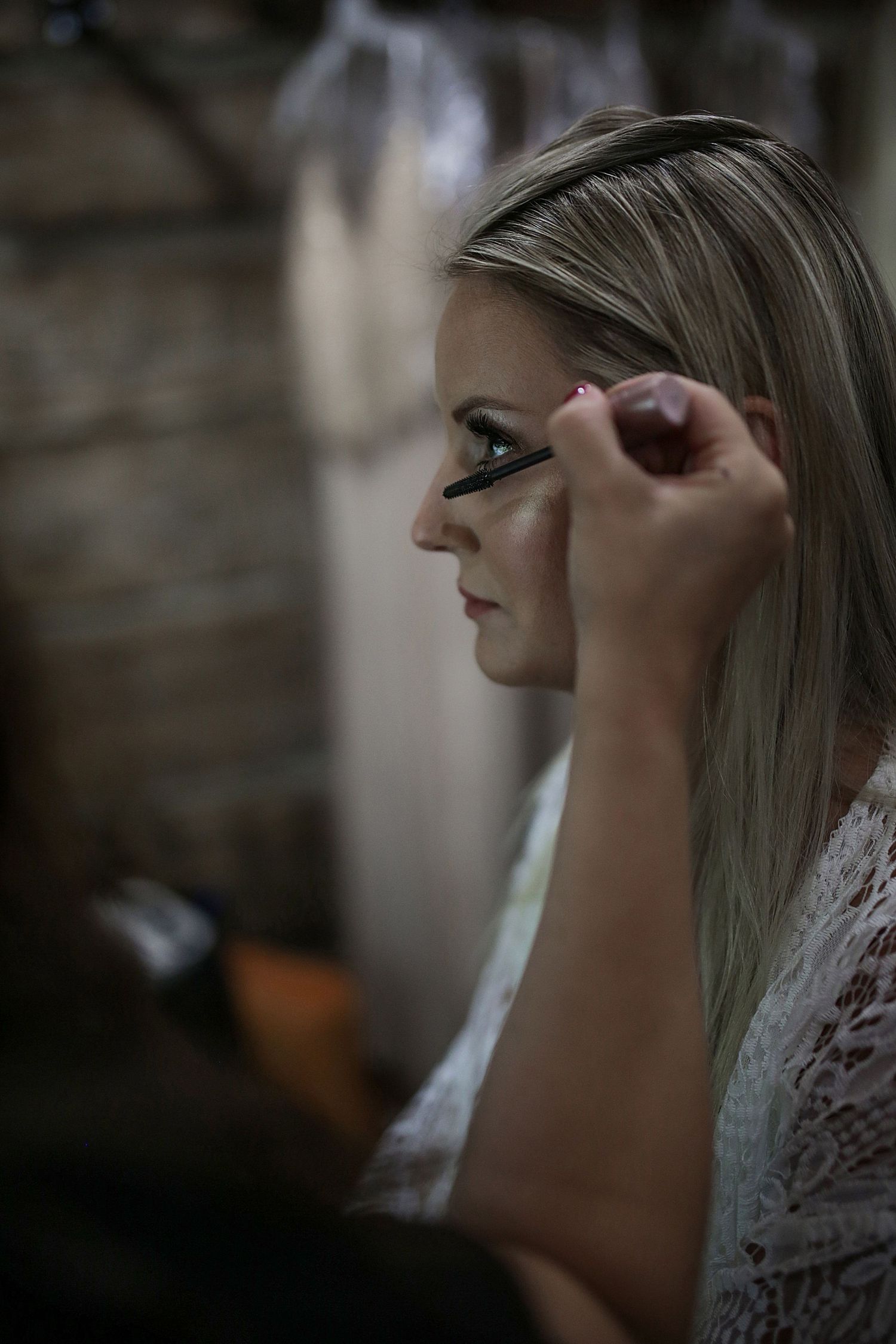 Makeup artist applies eyeshadow during bridal preparation in dramatic lighting.
