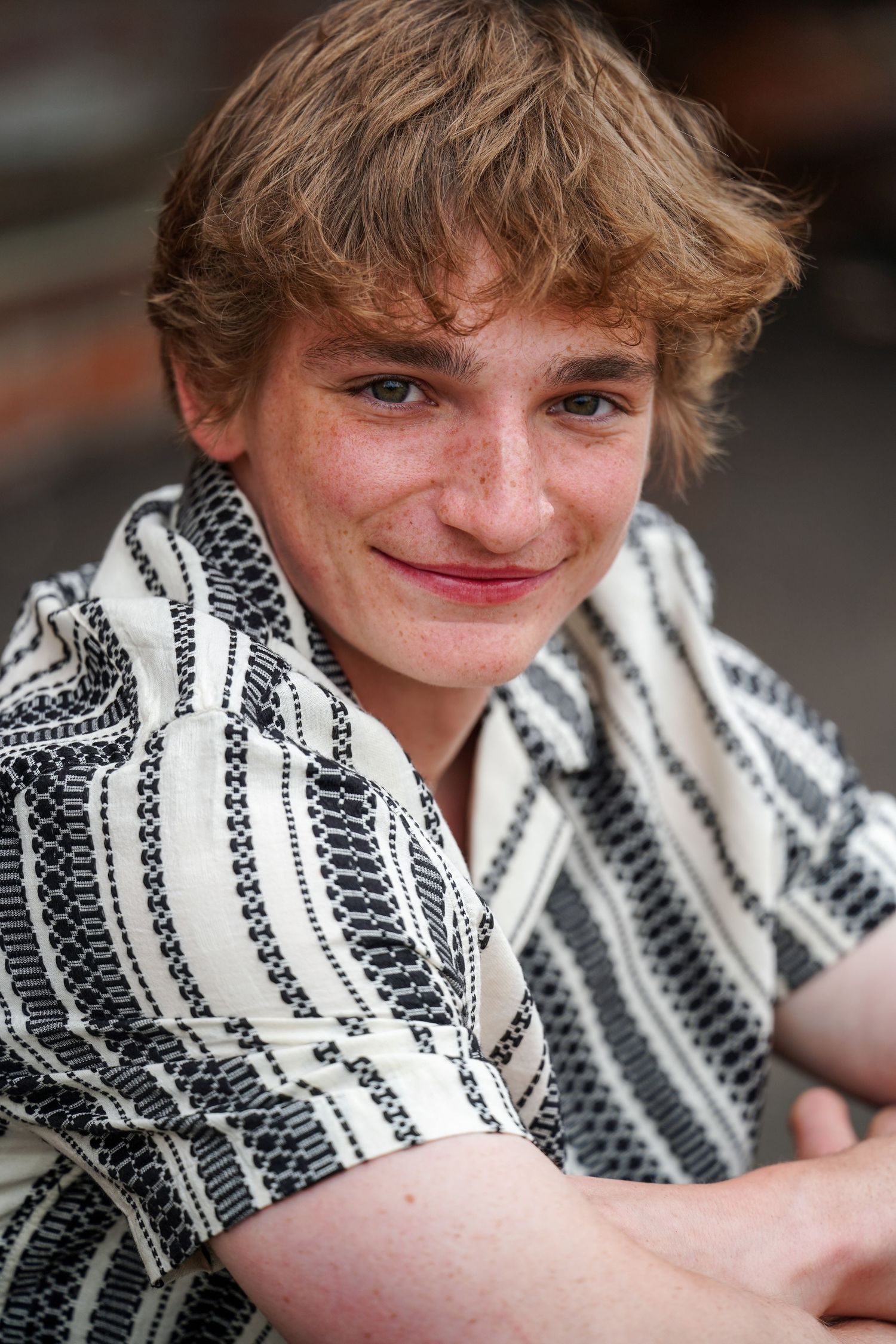 A person wearing a black and white striped button-up shirt smiles warmly at the camera in a casual portrait.