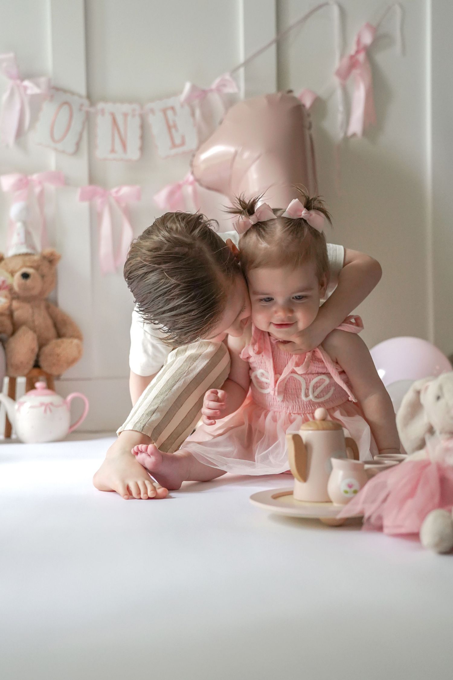 Pink tea party setting with banner decorations, teddy bear and balloons in soft pastel nursery decor.