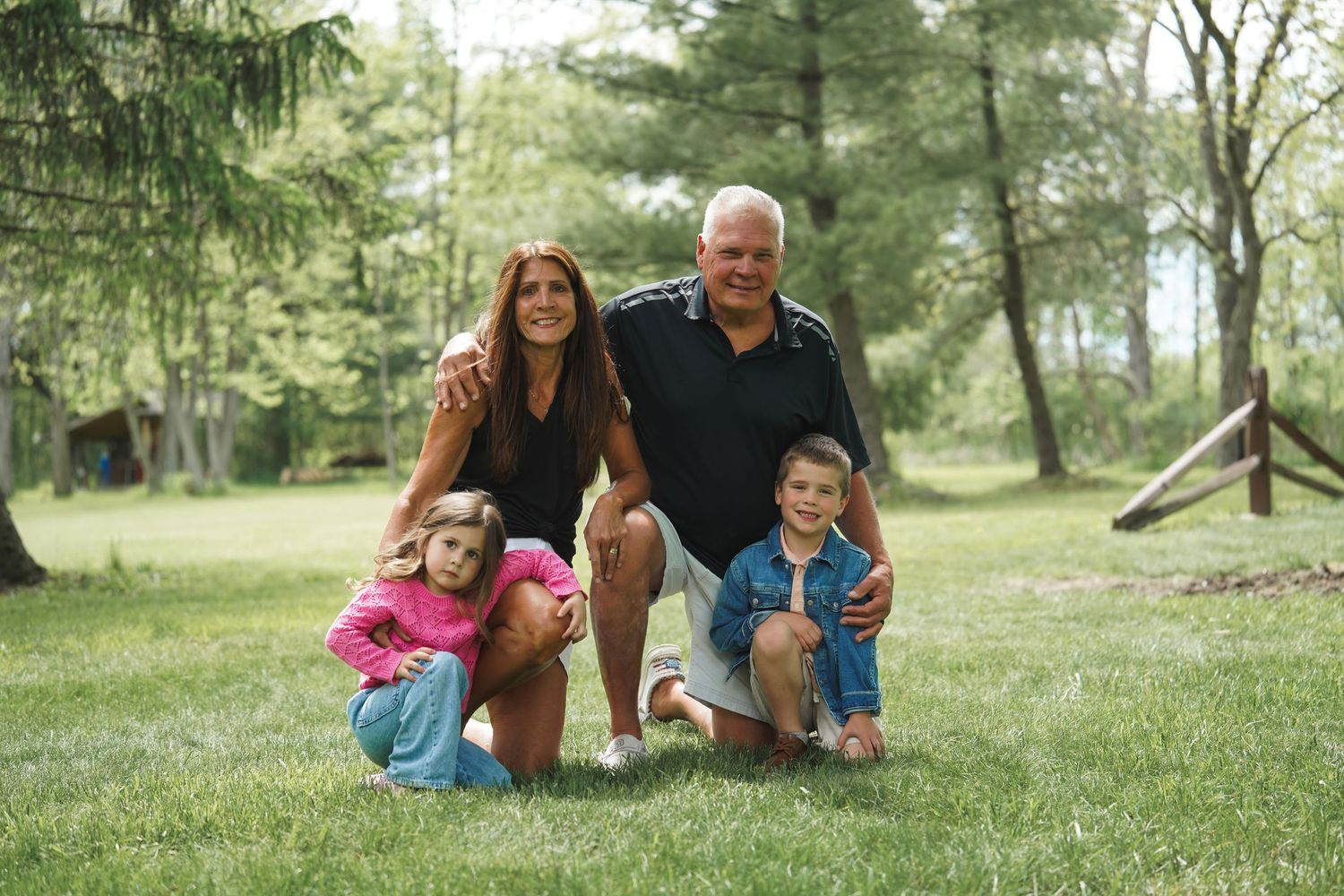 A family poses together on a grassy hill during a sunny afternoon in a park setting.