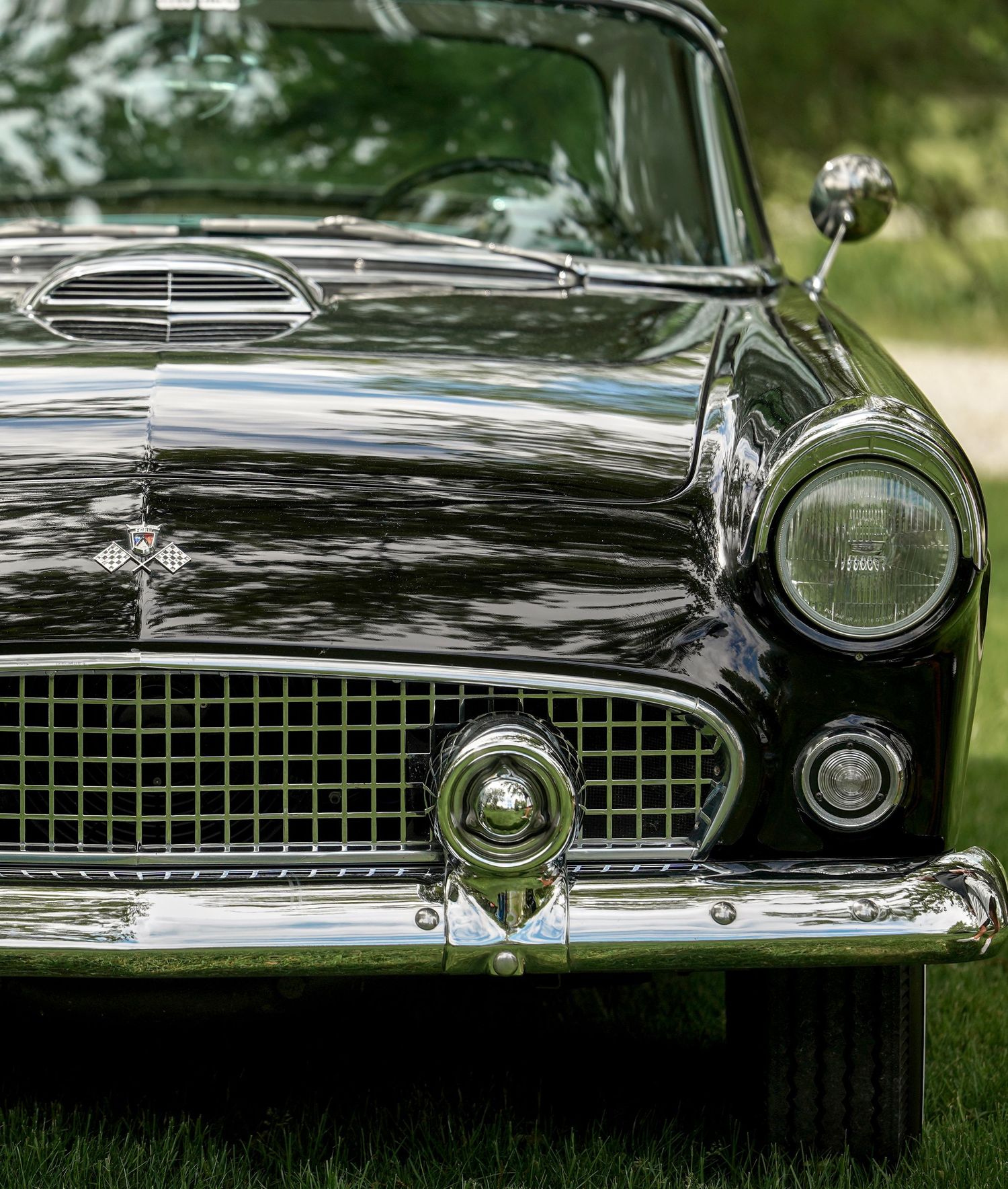 Close-up view of a classic black Ford Thunderbird front end showing chrome grille, headlight and polished finish.