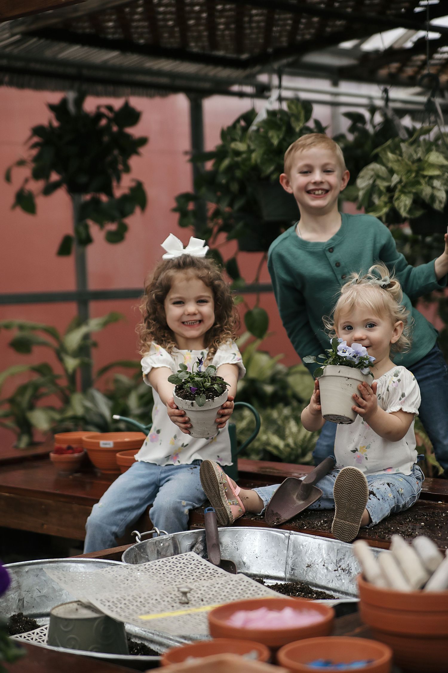 Children sitting at a rustic outdoor table engaged in gardening activities with potted plants and soil.