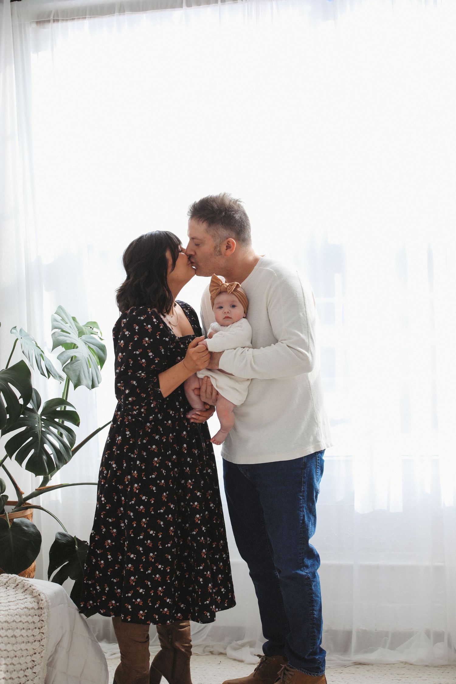 Three heartwarming photos of a family sharing tender moments together in a bright room with houseplants and white curtains.