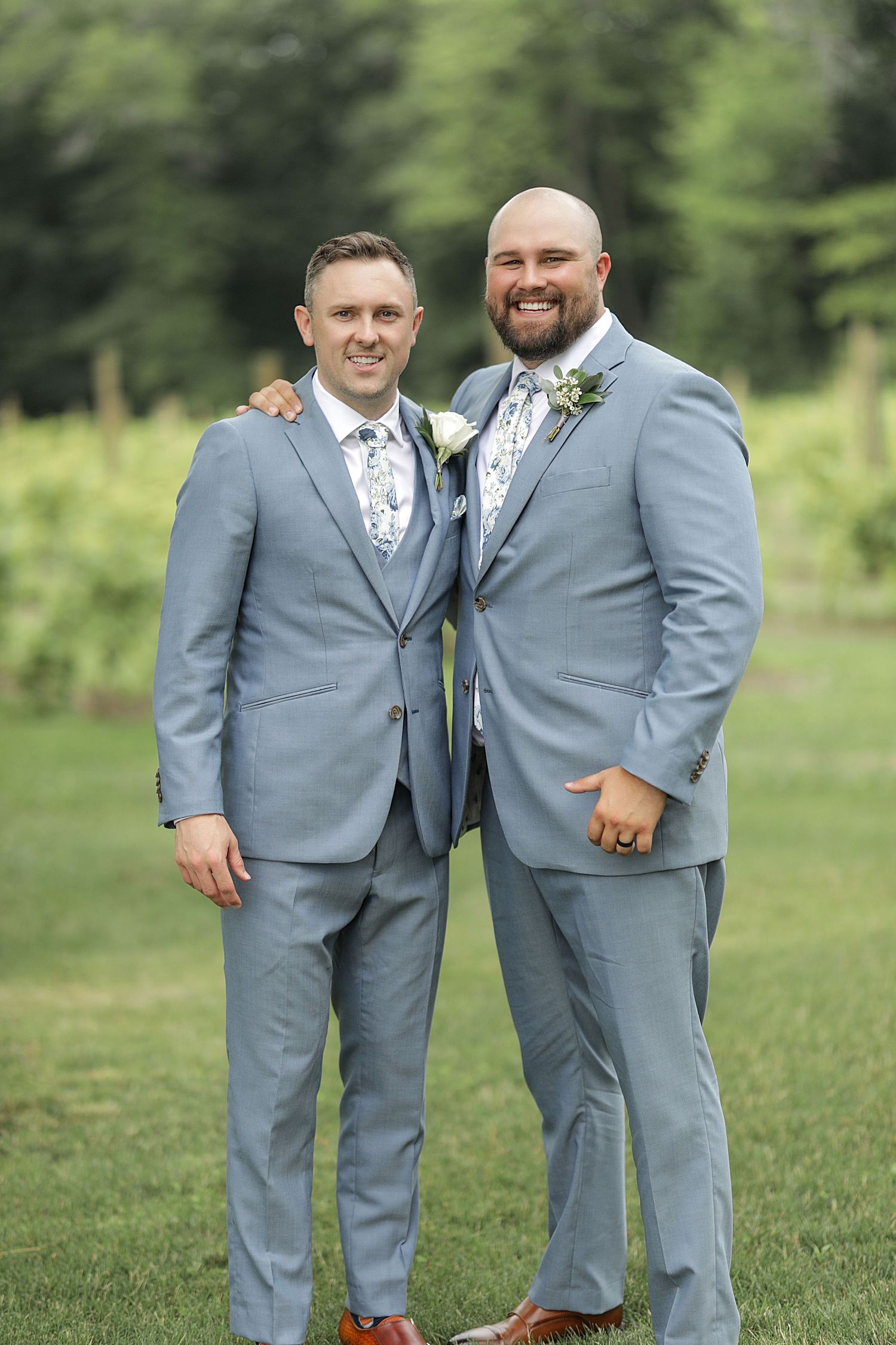 Two groomsmen in matching light gray suits share a friendly moment outdoors.