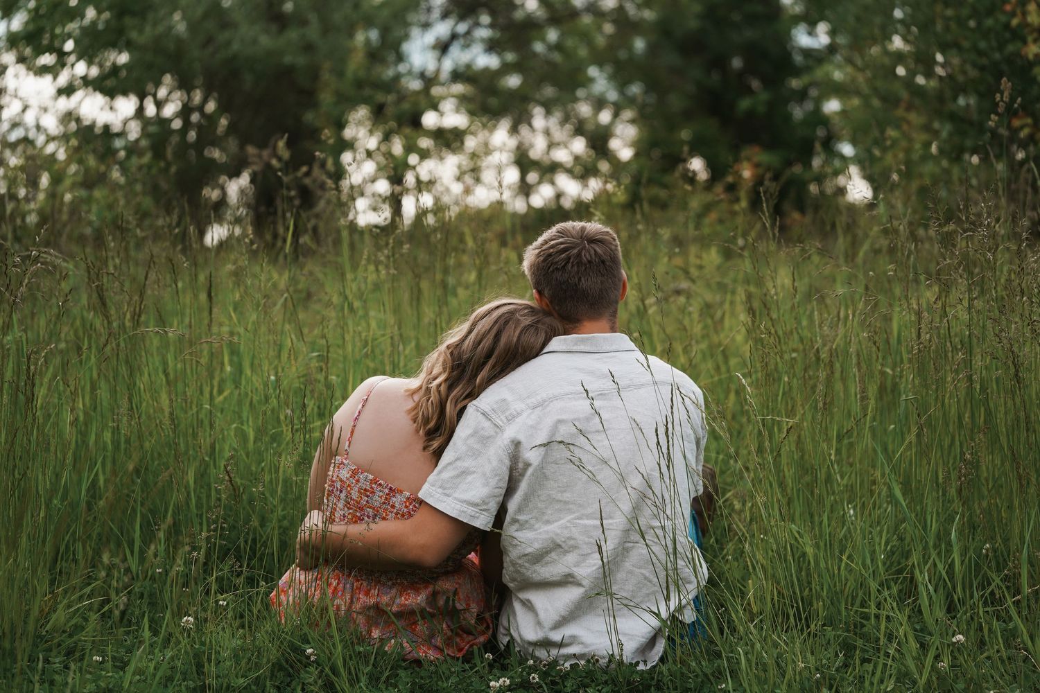 A couple sits together in tall grass during a peaceful moment in nature.