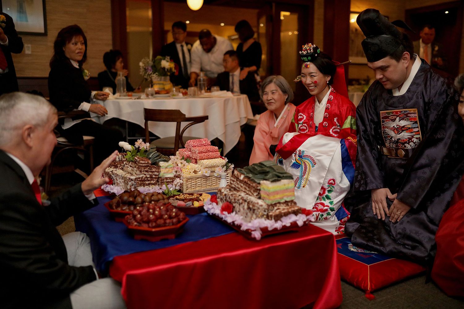 People gather around a table with holiday decorations and treats displayed on a red tablecloth at a festive event.