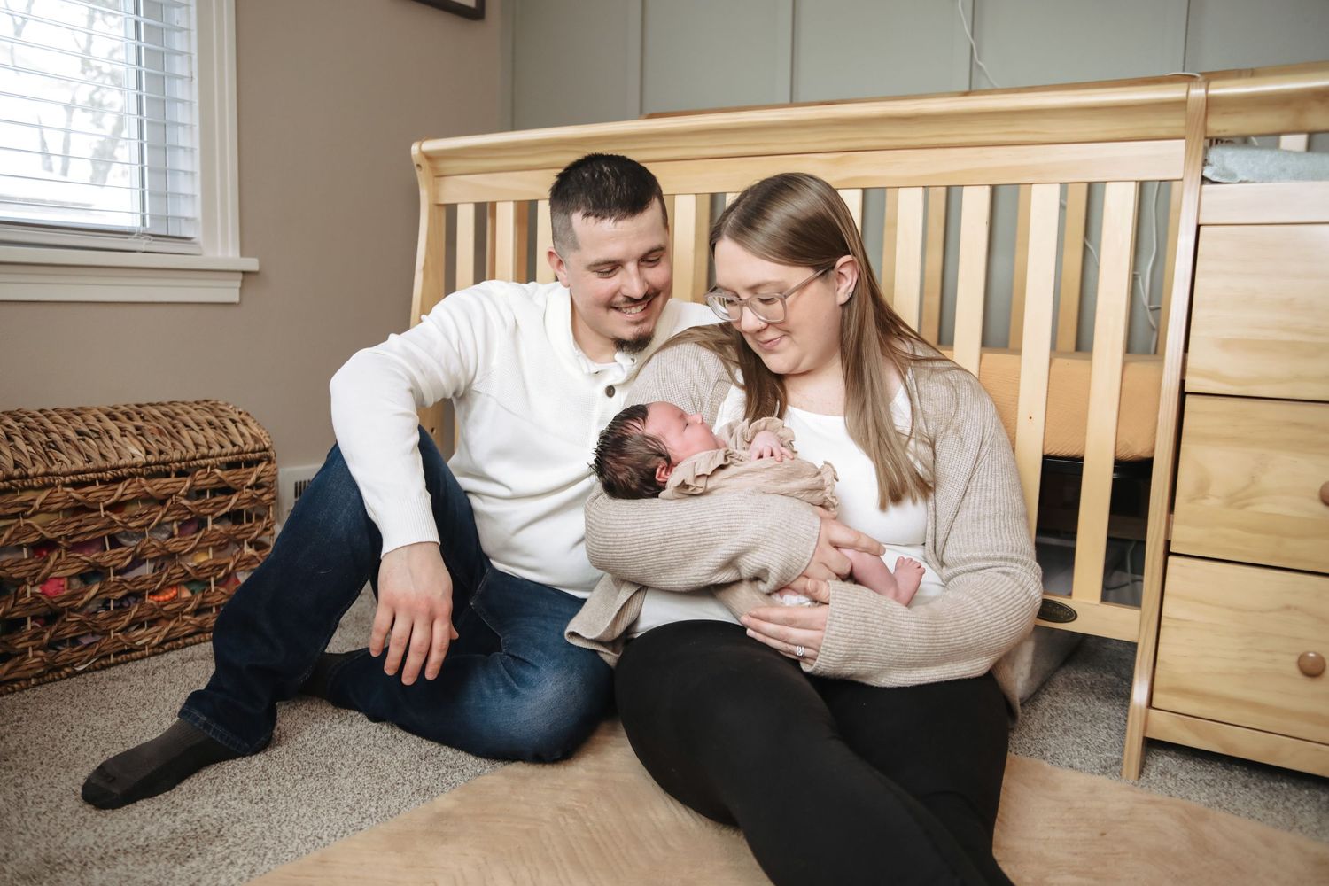 Family lying on carpet at home sharing tender moments with their newborn baby in casual setting.