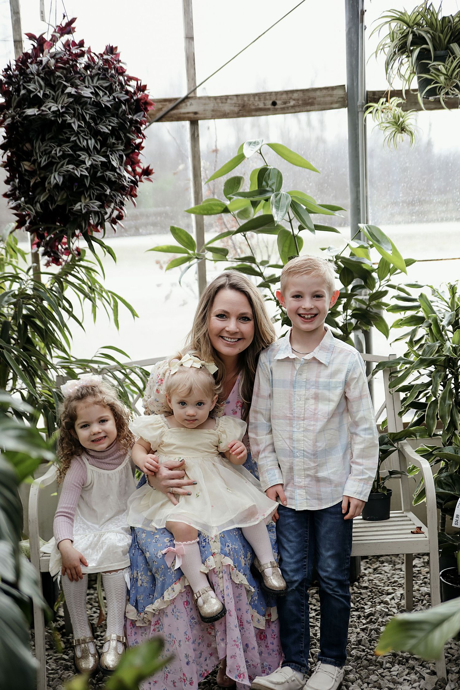 Children pose together inside a bright greenhouse surrounded by lush green plants and foliage.