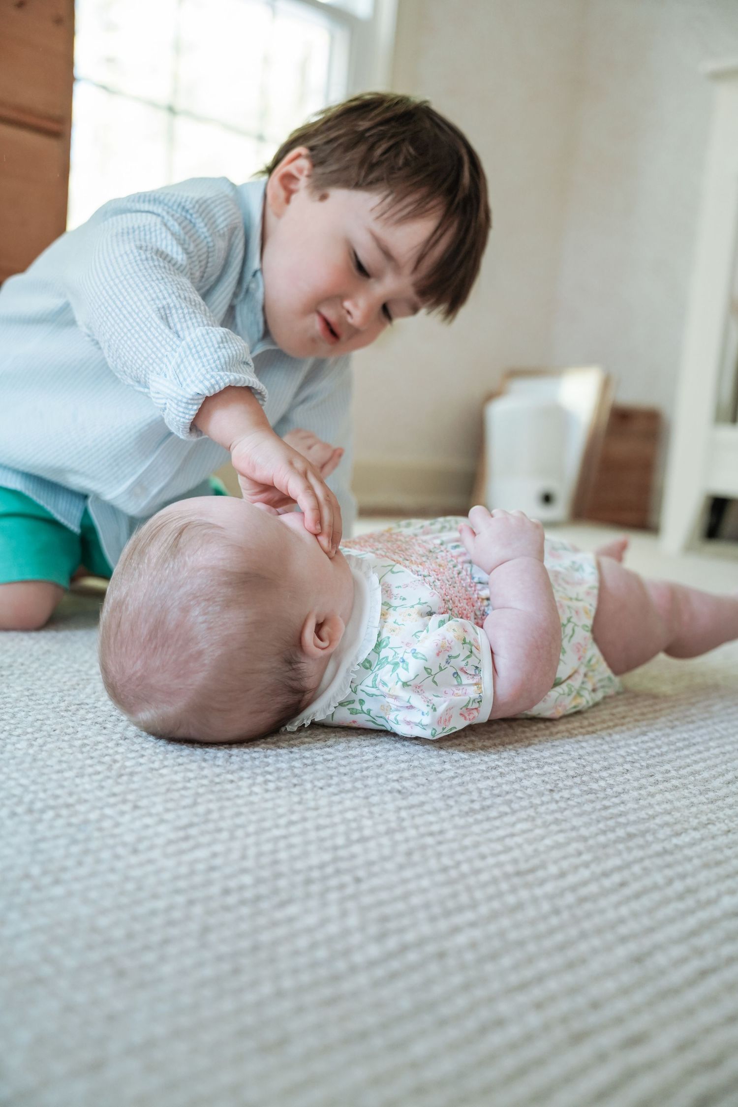 Three heartwarming photos show a young child interacting lovingly with a baby on a carpeted floor.