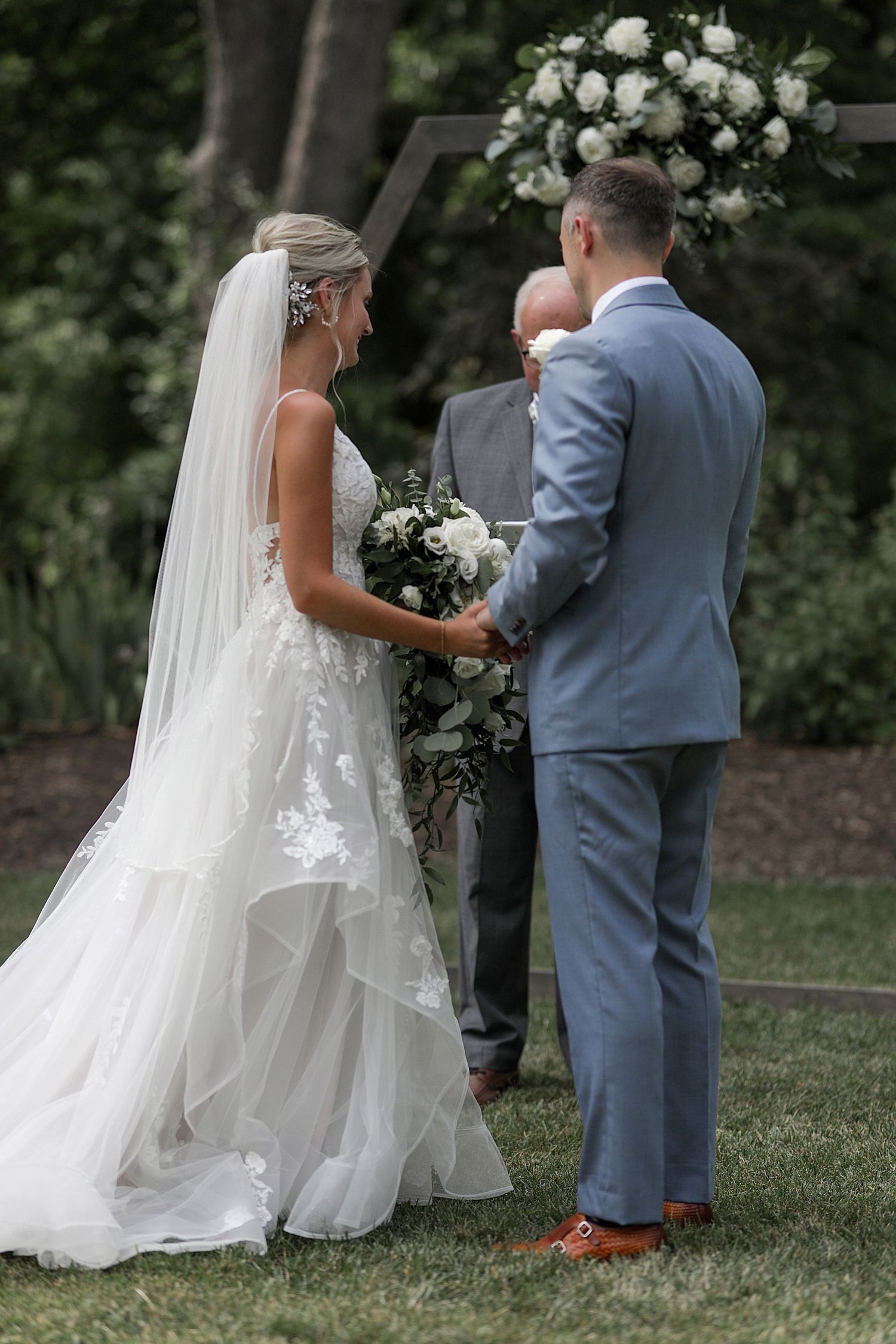 Wedding ceremony in garden setting with couple and officiant at floral-decorated altar.