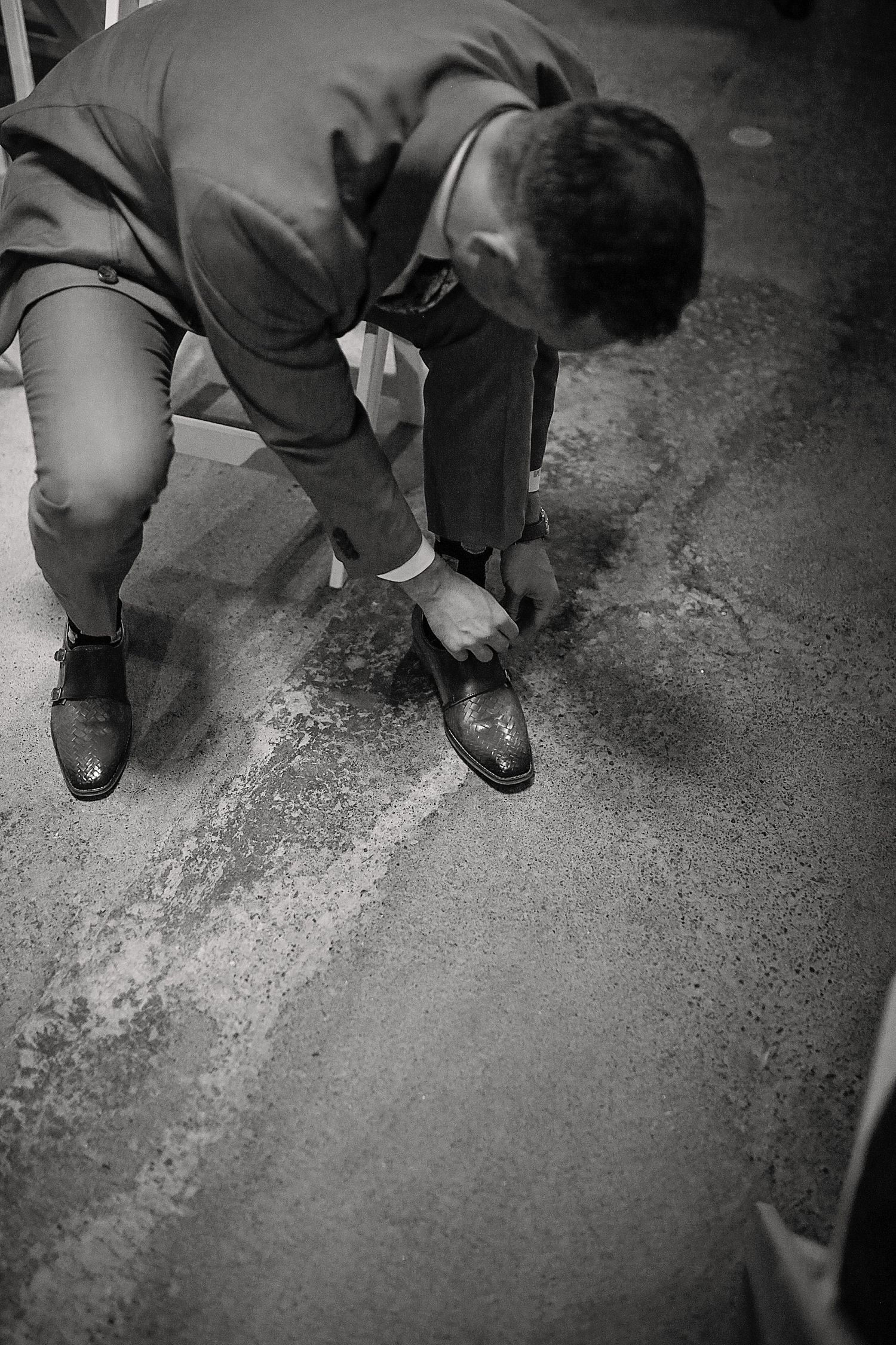 Black and white photo of someone tying dress shoes while getting ready.