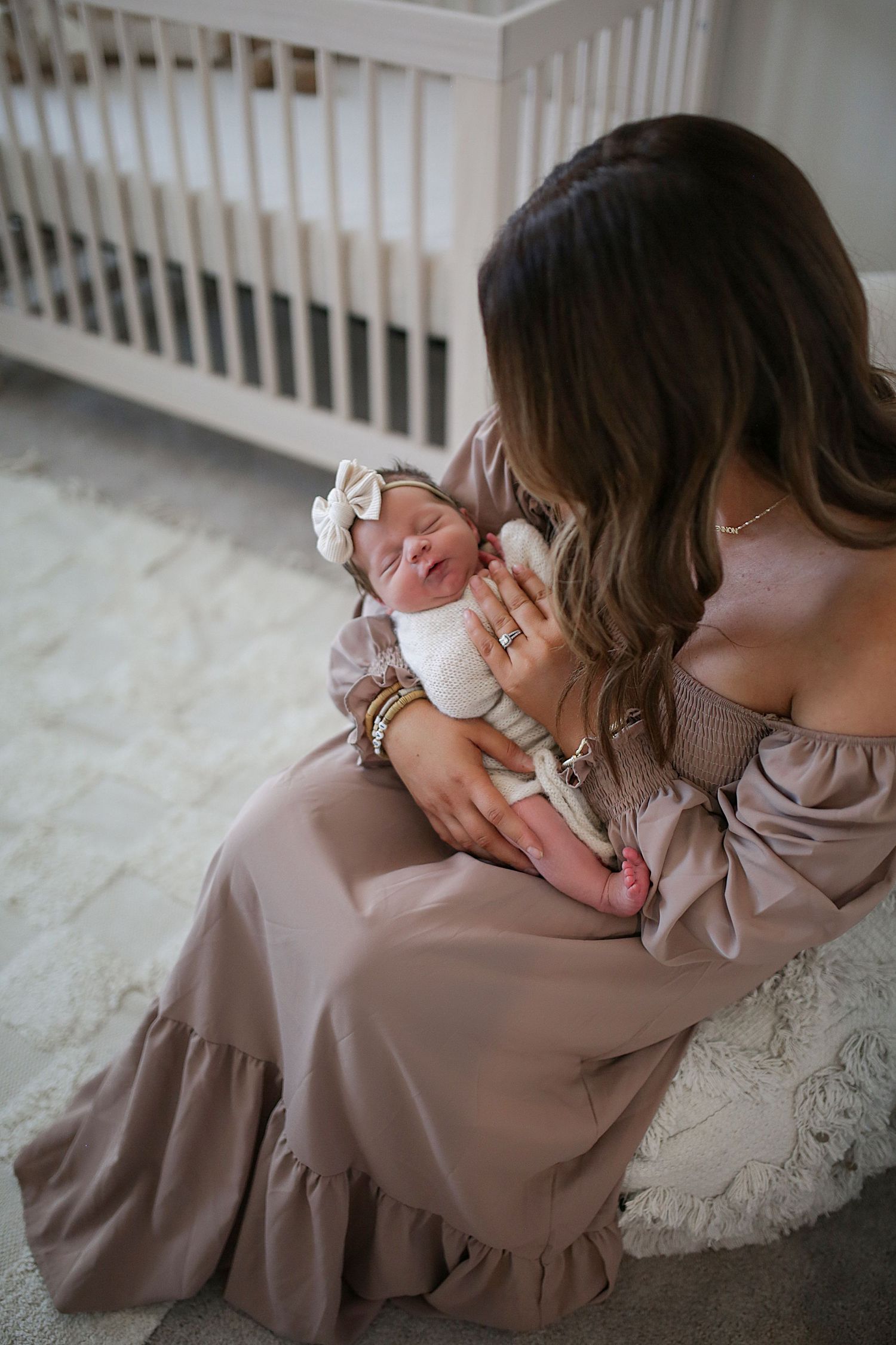 A crying newborn baby being comforted in a nursery room with a white crib in the background.