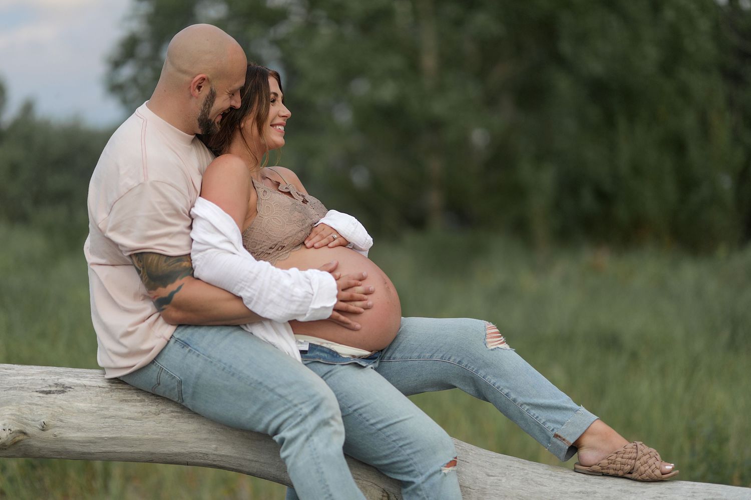 A couple sits in a green meadow enjoying an intimate outdoor moment together at golden hour.