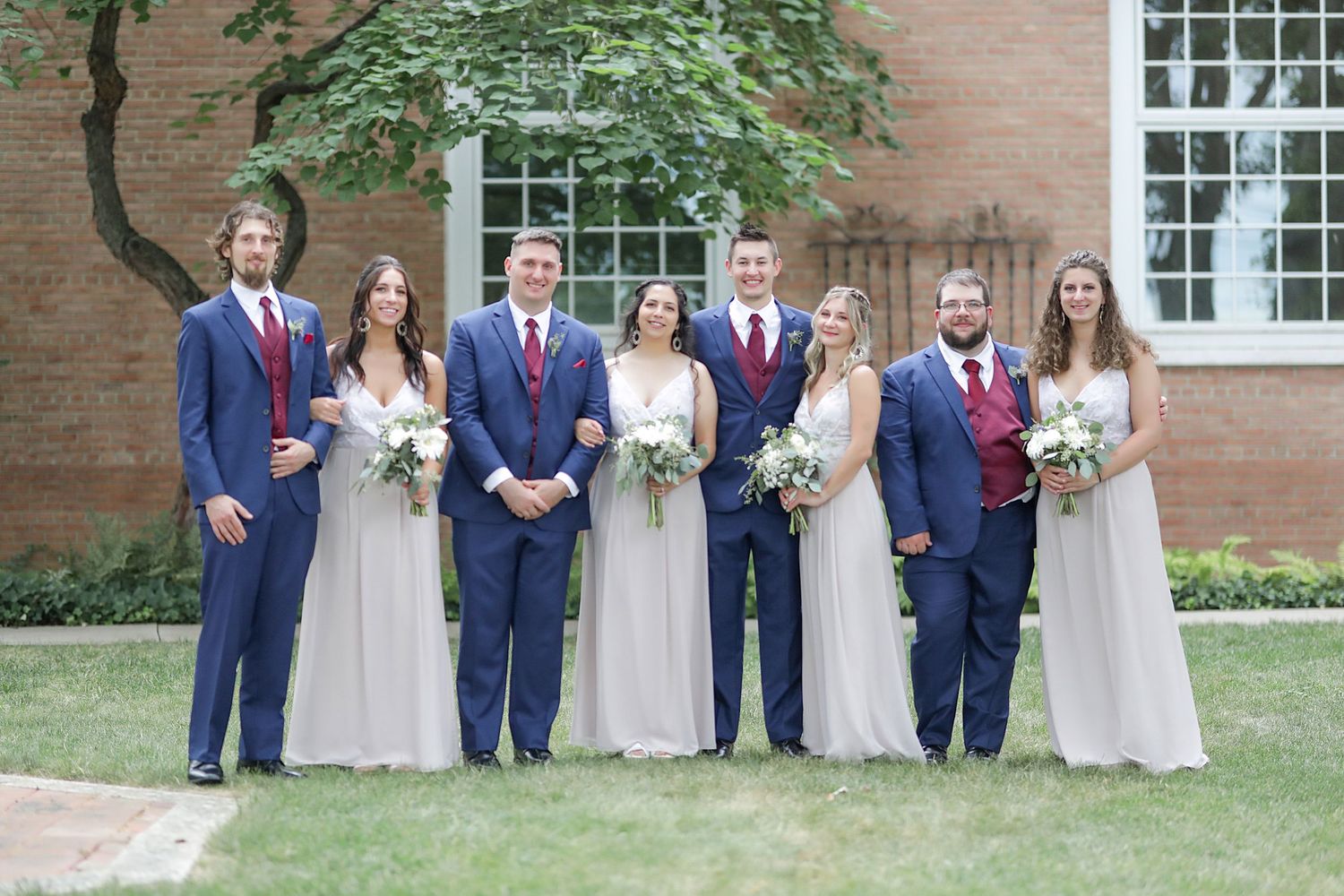 Wedding party in navy blue and blush poses in front of brick building on sunny day.