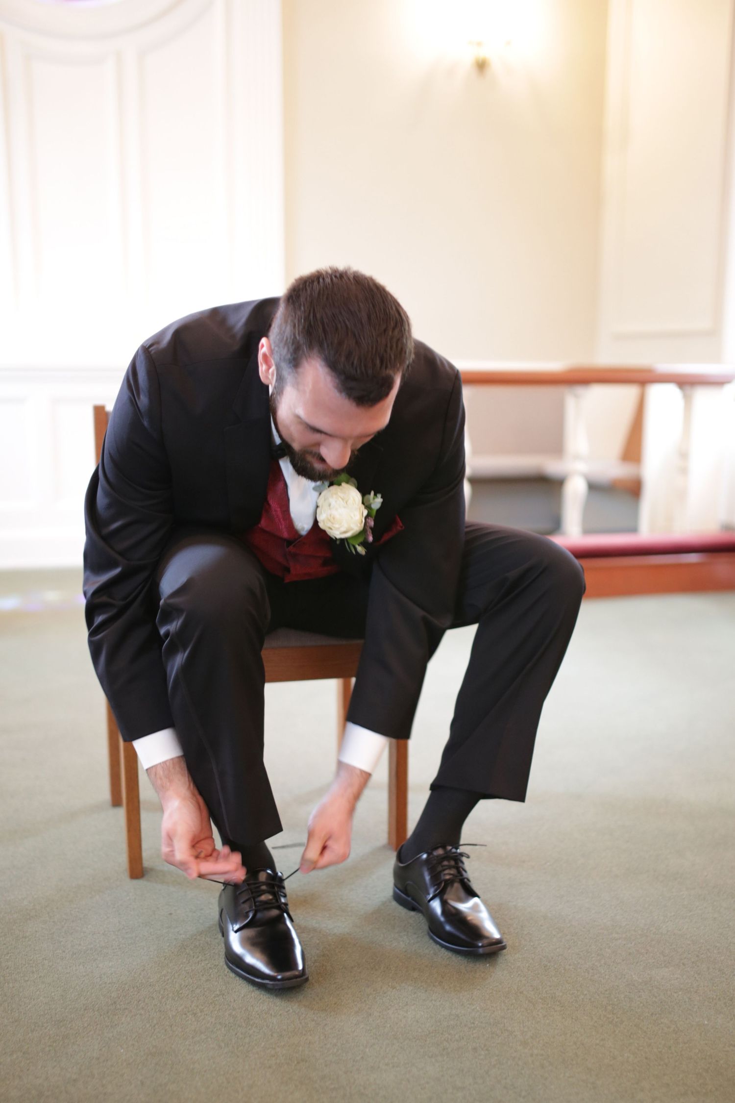 Well-dressed groomsman in black tuxedo bends down to adjust his formal black dress shoes.