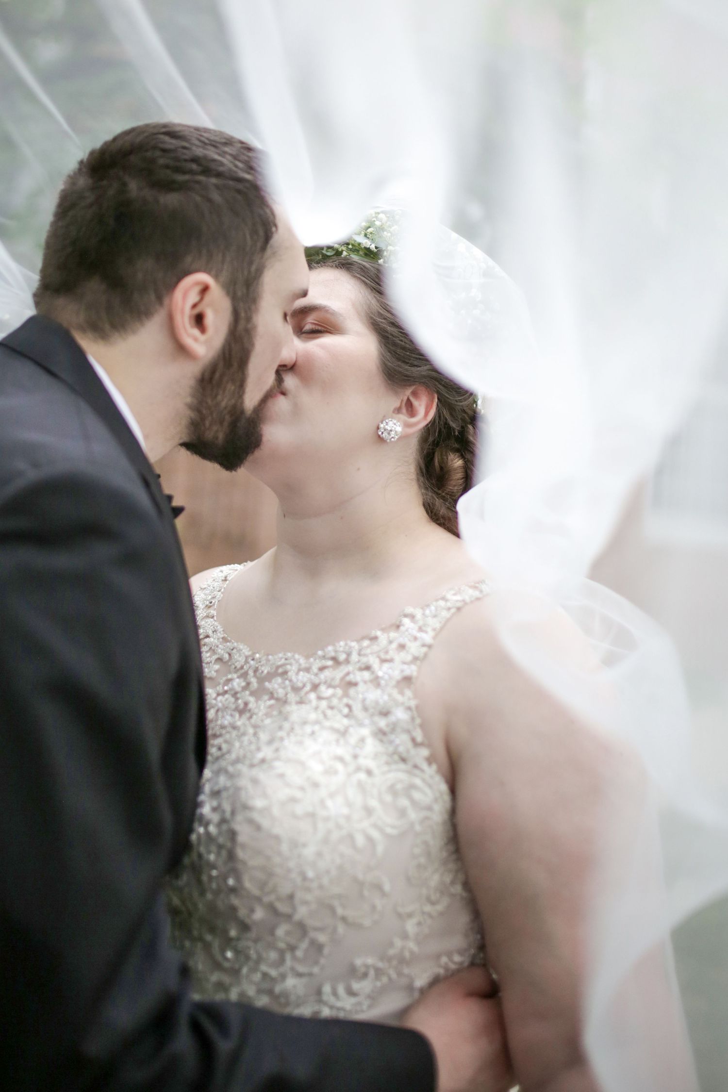 A romantic wedding kiss captured through a soft veil, with the bride wearing an elegant beaded lace dress.
