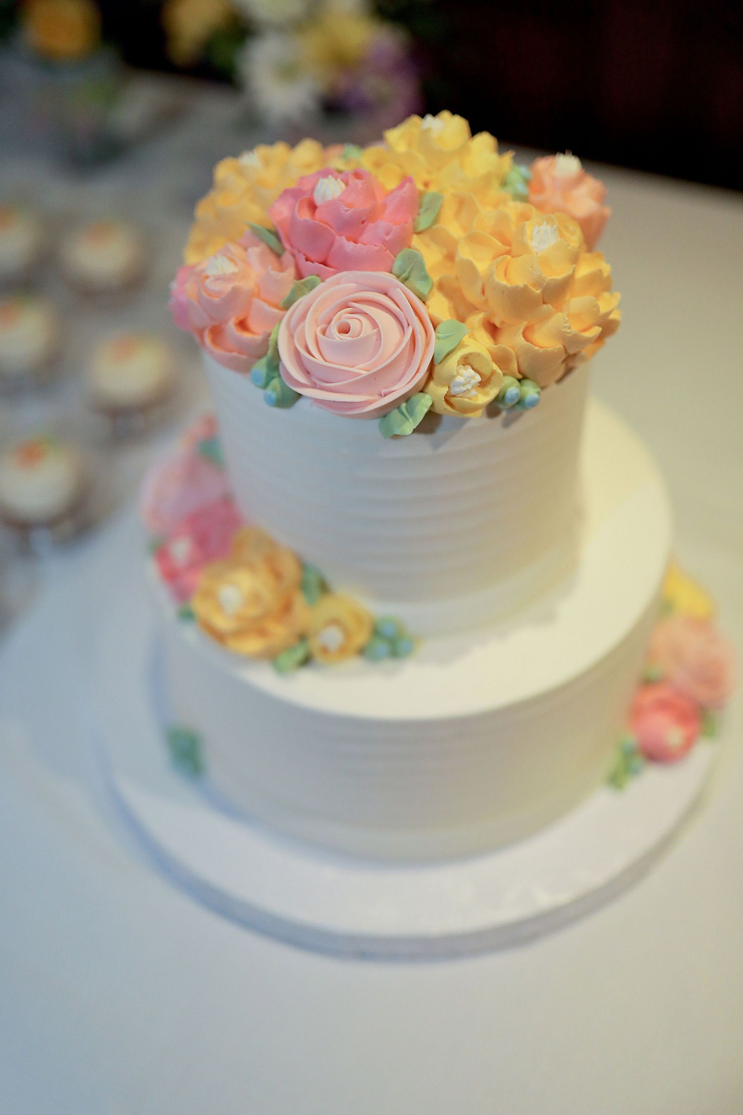 Elegant two-tier white wedding cake decorated with delicate pink and yellow sugar flowers on a light blue tablecloth.
