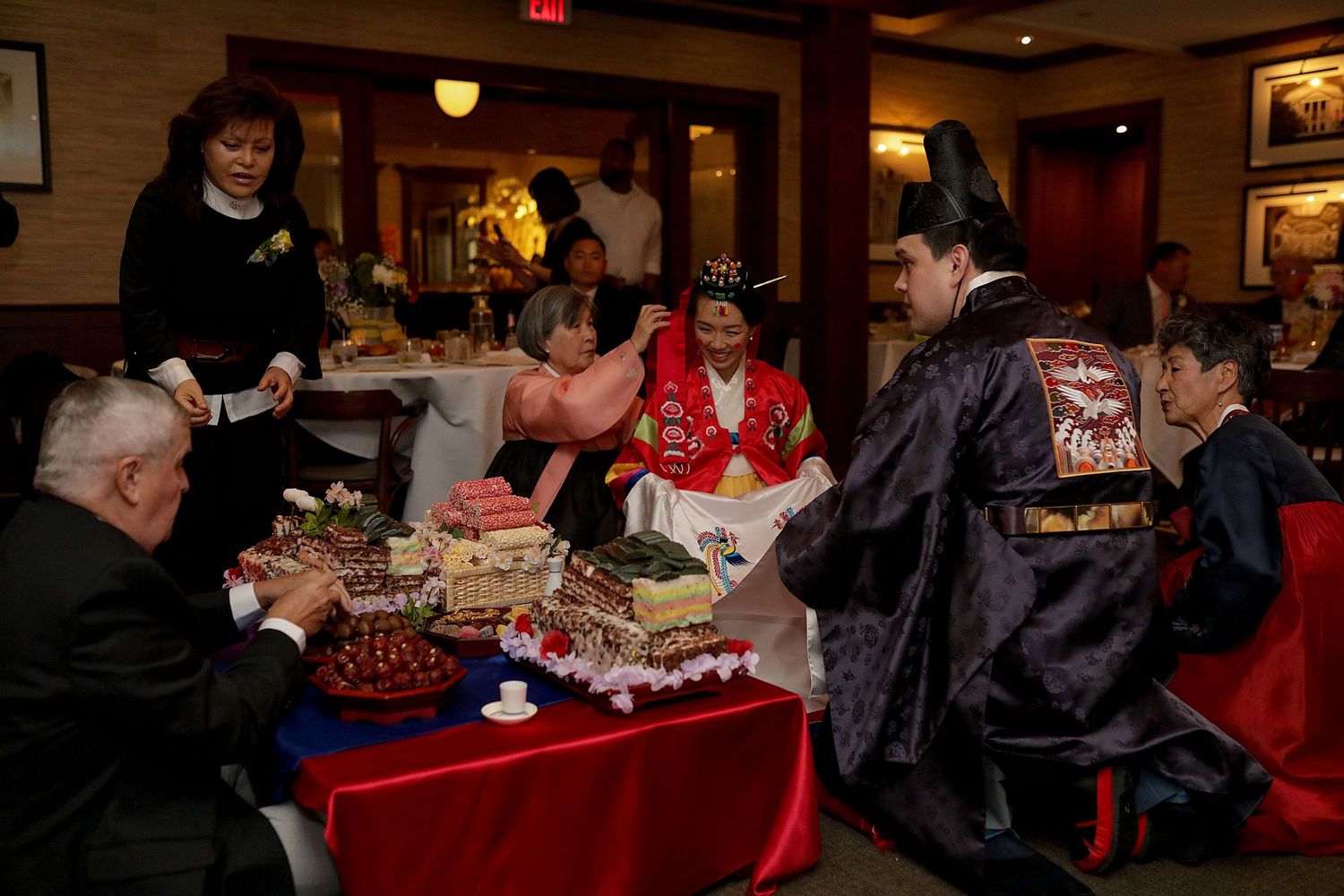 People enjoying a social gathering around tables with desserts and refreshments at an indoor event.