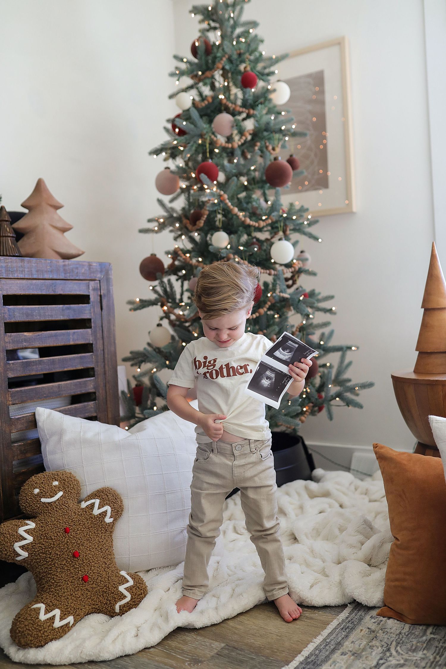A small child sits on a white blanket near a decorated Christmas tree and gingerbread decorations.