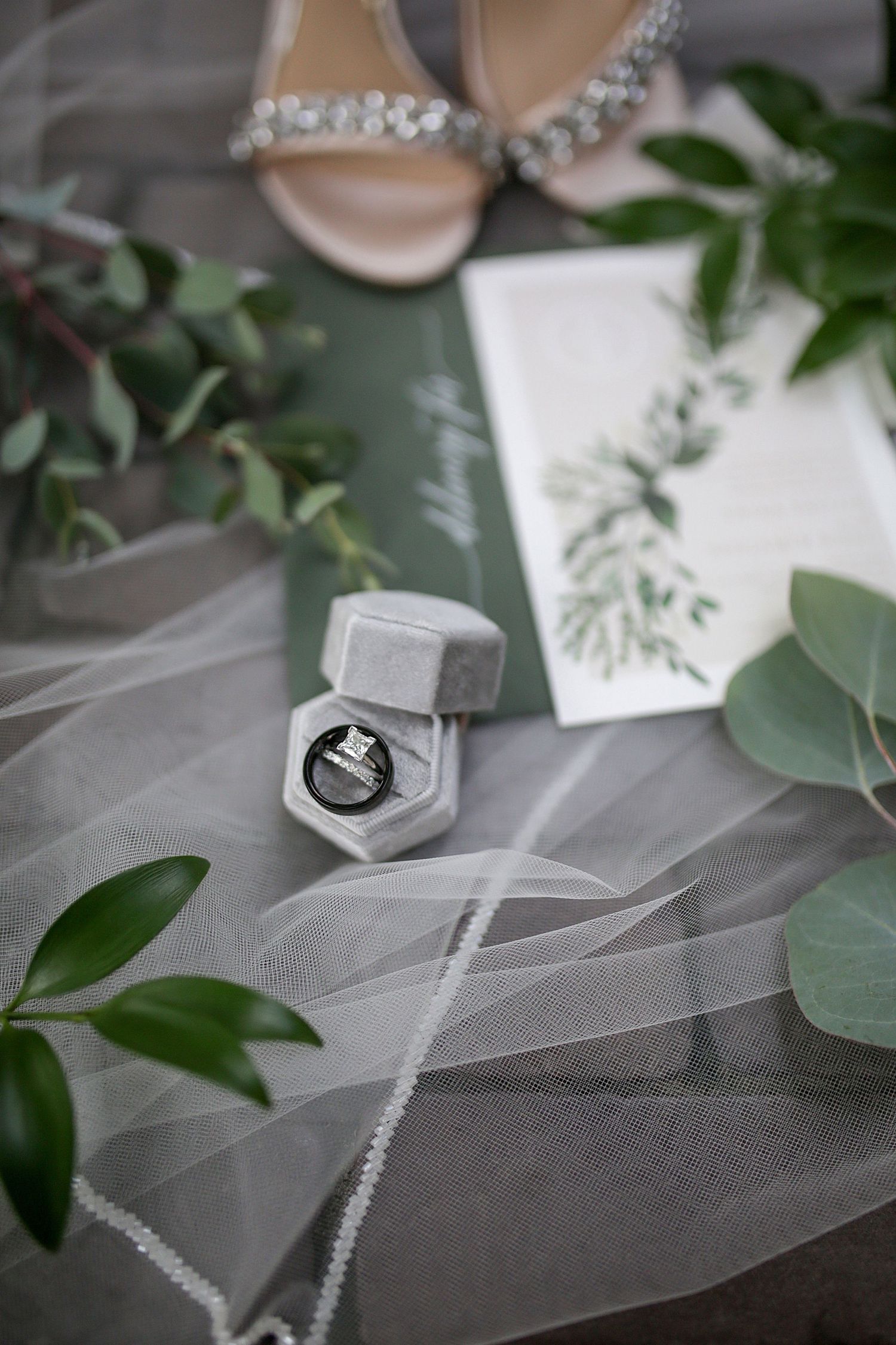 Wedding ring in gray velvet box with veil and greenery styled on white surface. Cleveland wedding photographer.