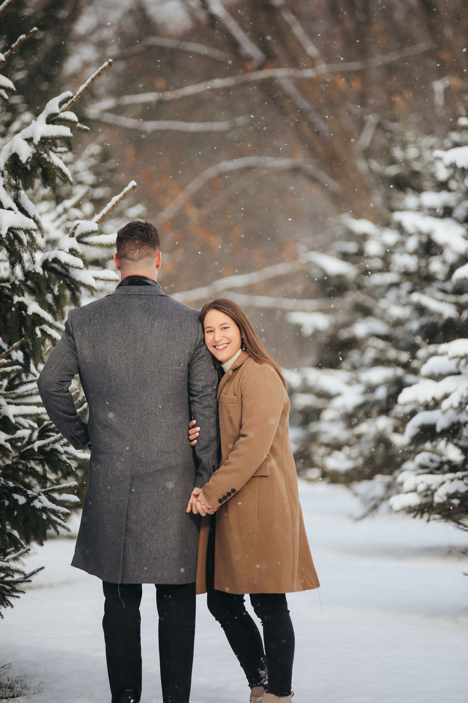 A couple shares a romantic moment in a snowy winter landscape surrounded by evergreen trees.