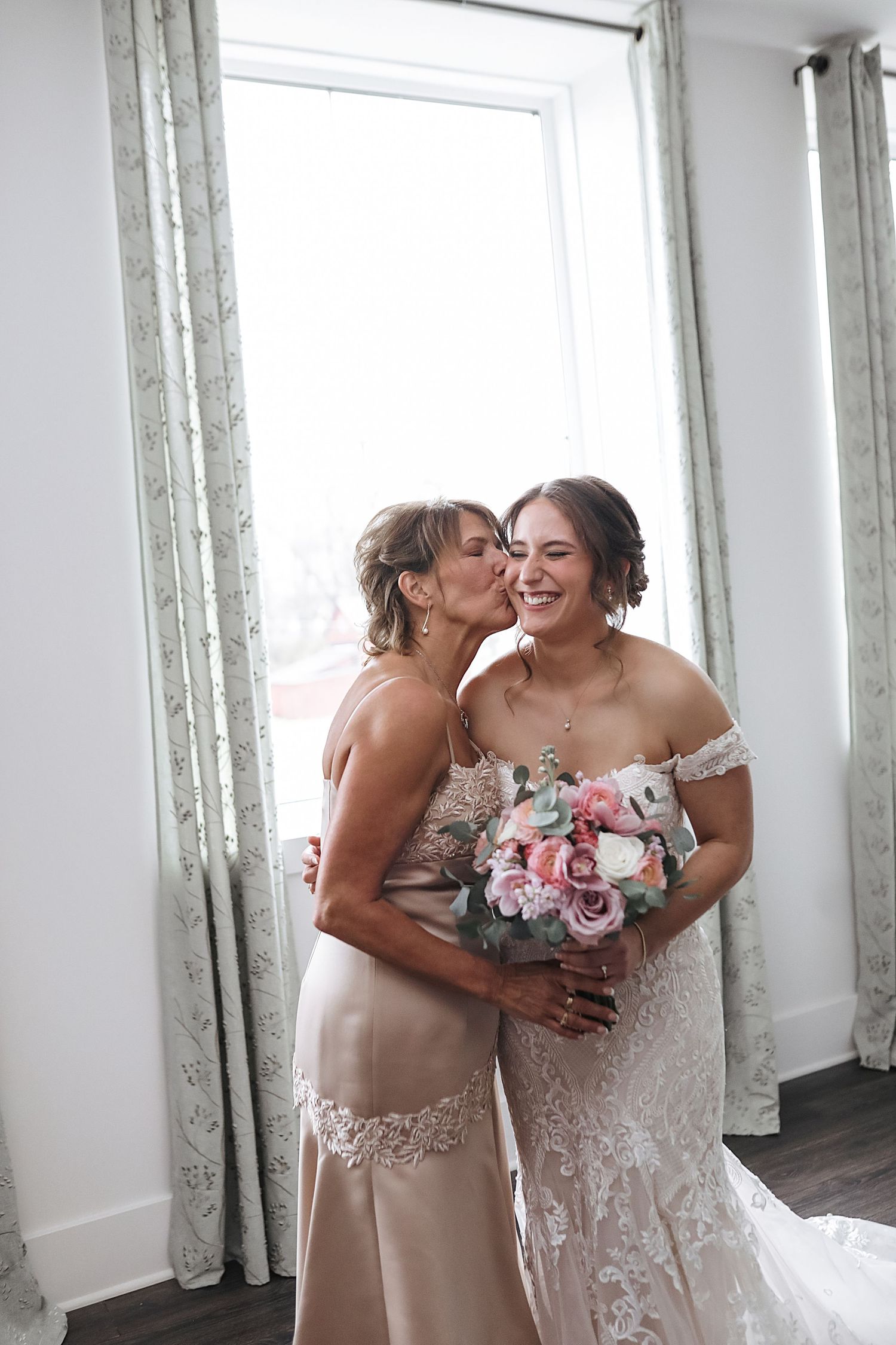 A heartwarming candid moment captured between two people in elegant dresses holding floral bouquets.