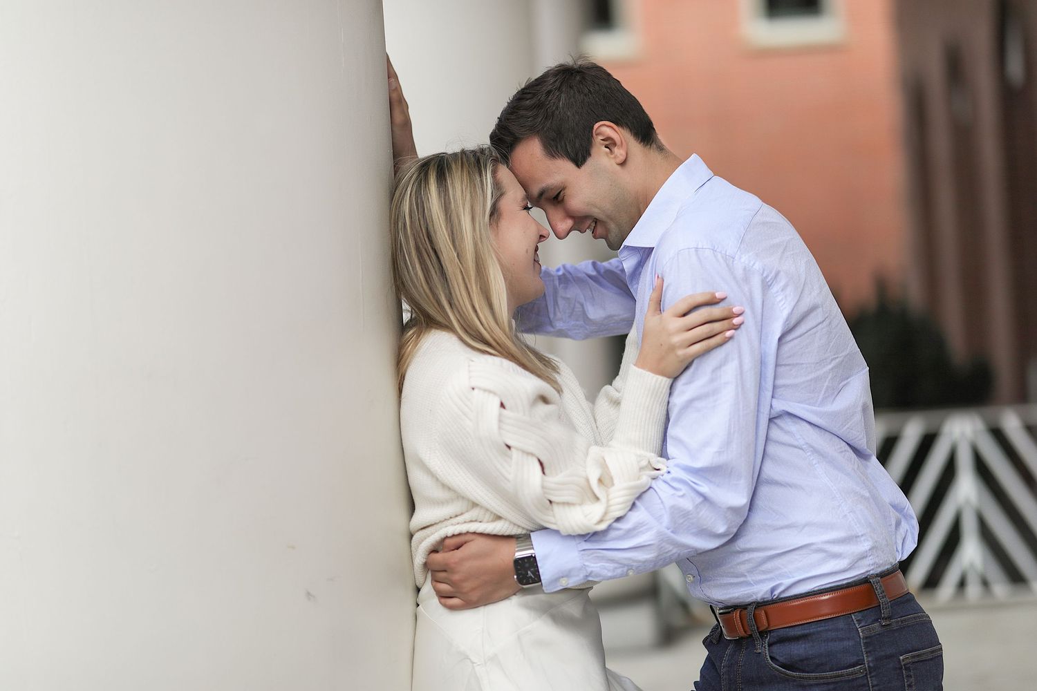 Two people in formal attire share a tender embrace while standing outside a brick building.