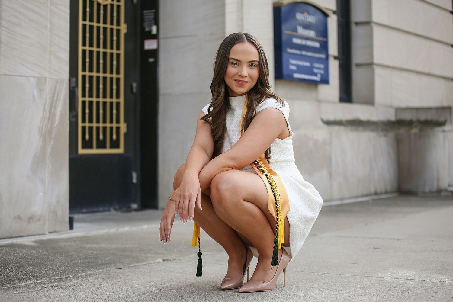 A person in a white dress sits and poses on stone steps outside a building entrance.