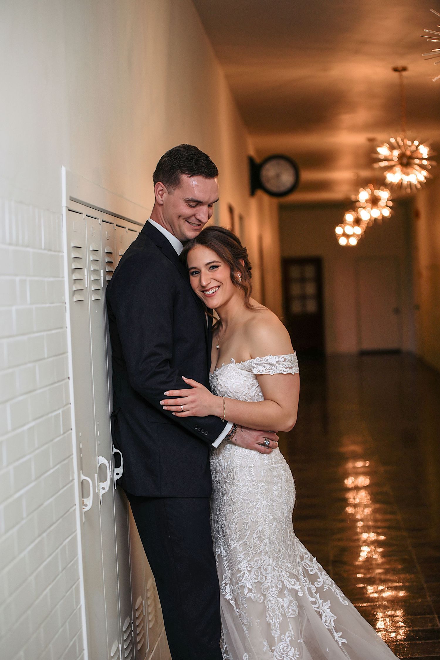Newlywed couple shares romantic moments in a white hallway with glowing wall sconces creating warm ambiance.