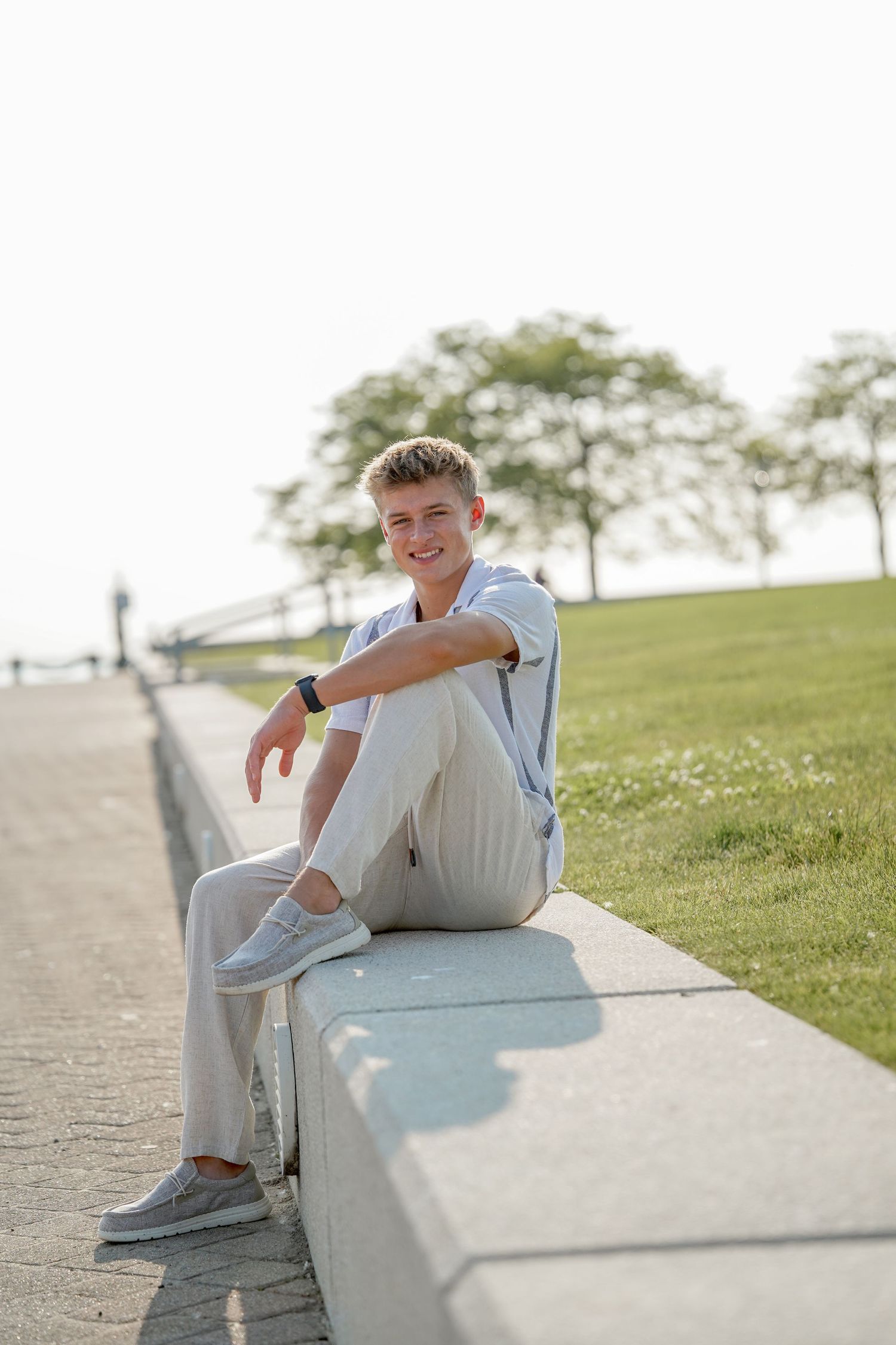Young person relaxing on concrete steps wearing light colored clothing outdoors on a sunny day.
