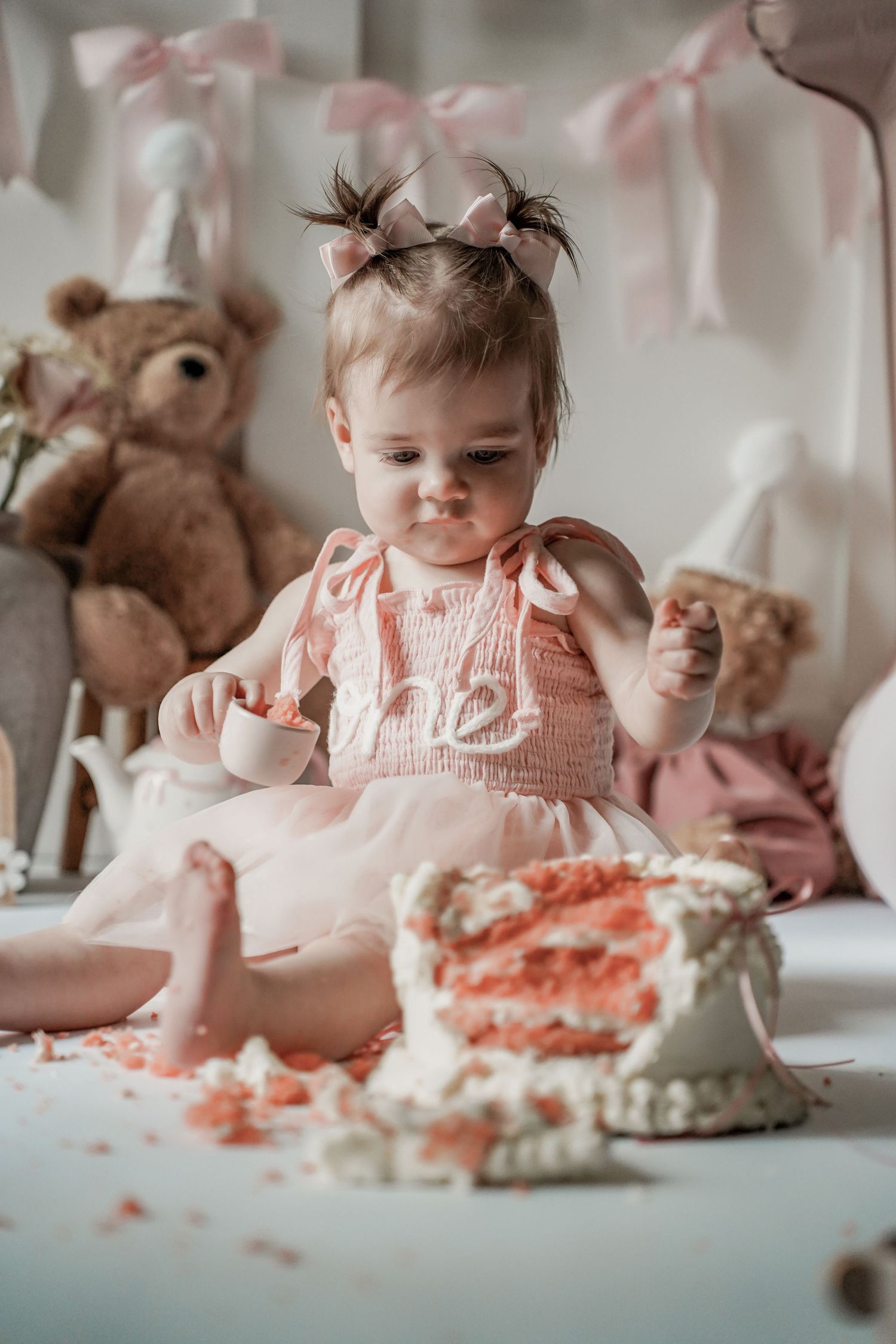 Four sequential photos showing a baby in pink exploring and playing with a smashed birthday cake on a white table.
