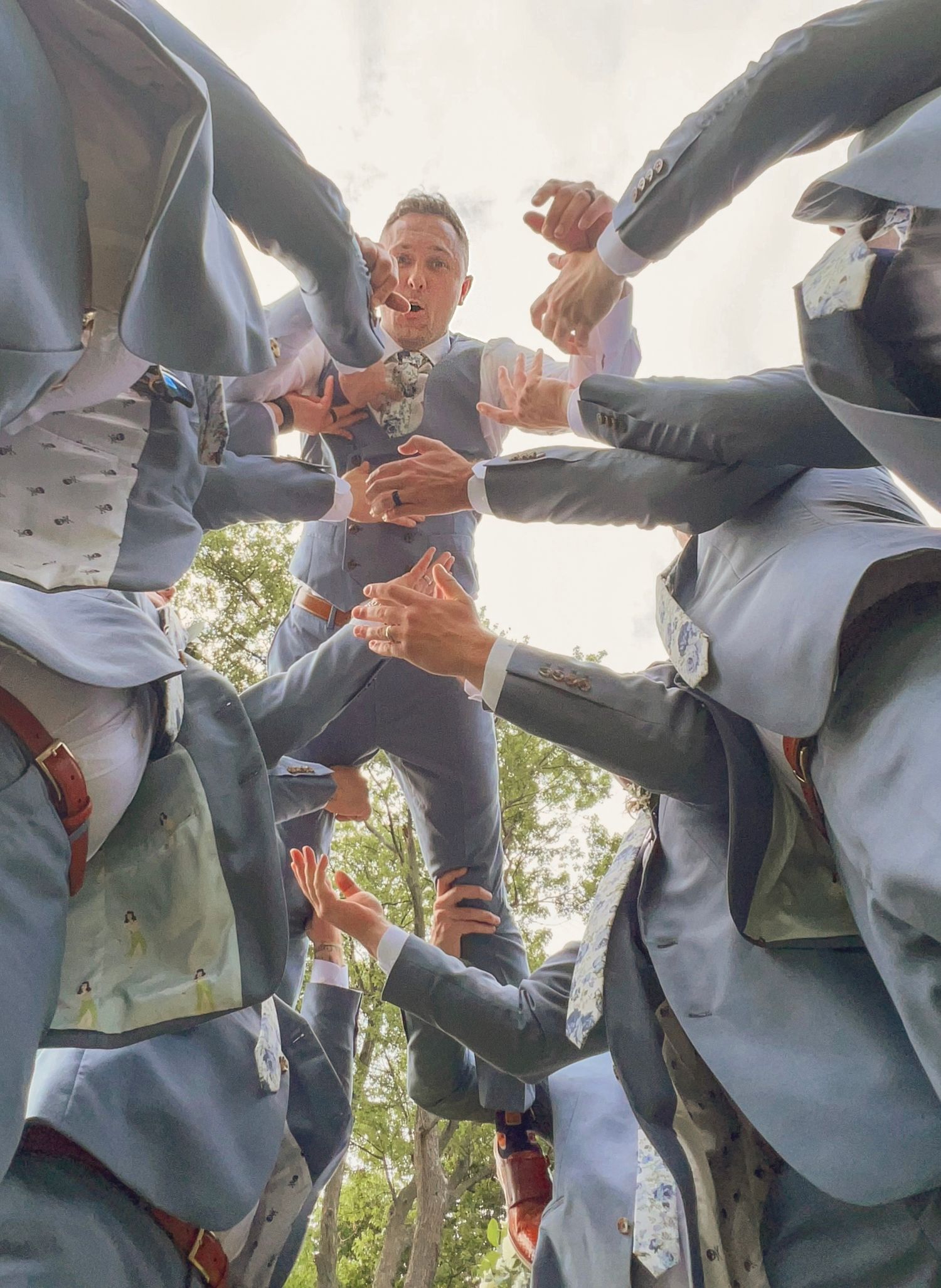 Groomsmen in gray suits show off their matching brown leather accessories.
