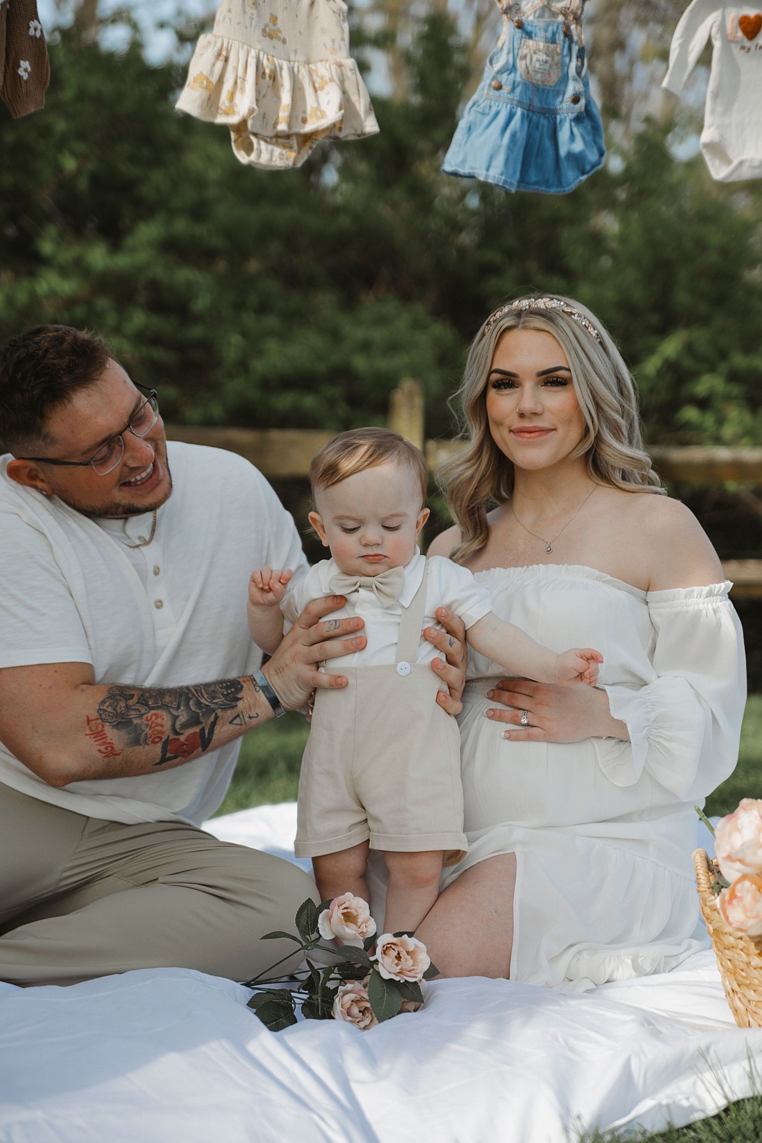 Family enjoys a picnic outdoors with vintage dresses hanging above on a sunny day.