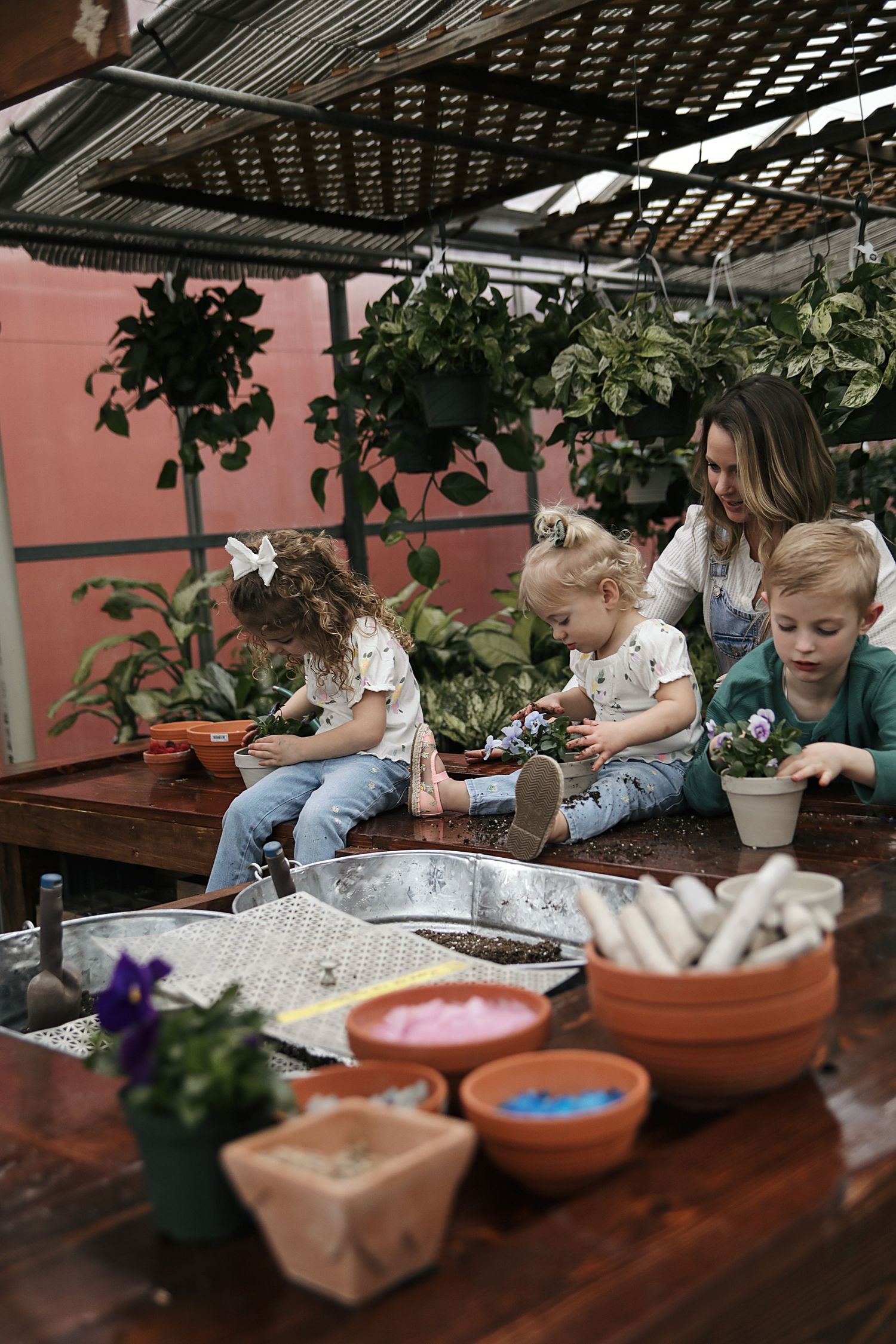 Children gather around a wooden table working on arts and crafts activities with plants and colorful supplies nearby.