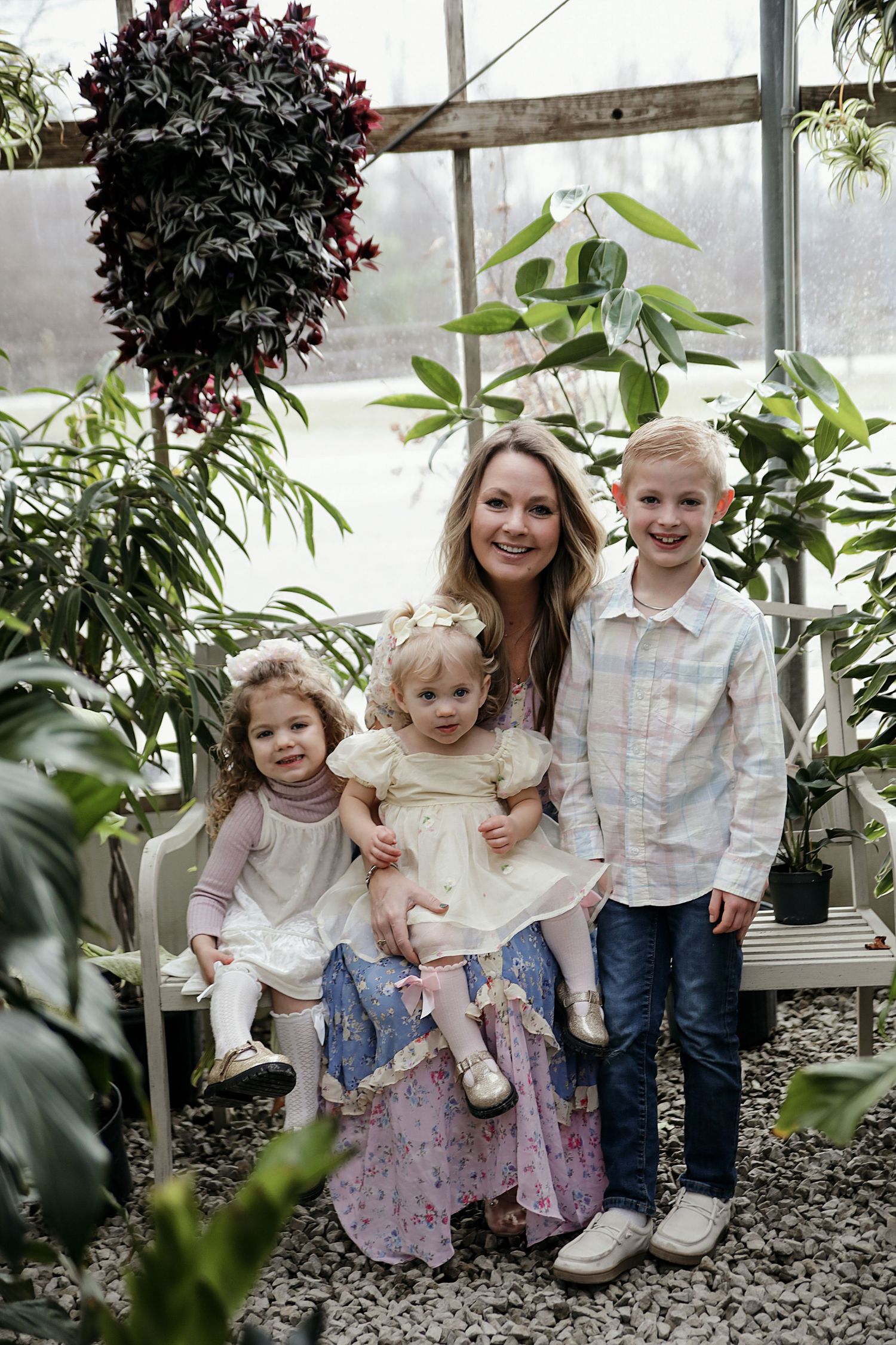 A greenhouse setting with a family group posing together among lush plants and greenery.