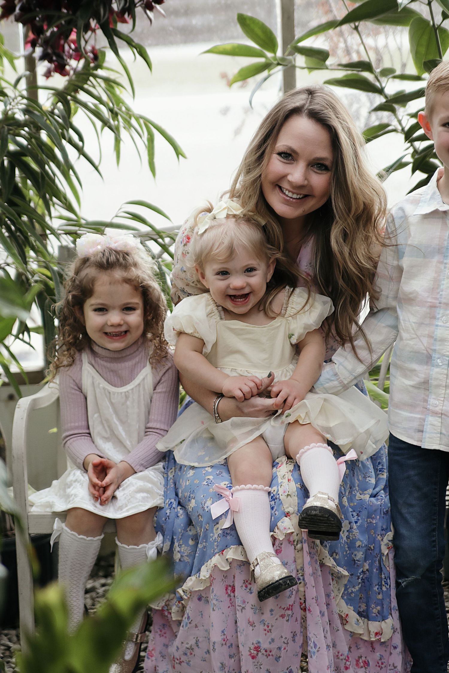 A mother and daughter share playful bonding moments in a garden setting wearing floral skirts and light colored tops.