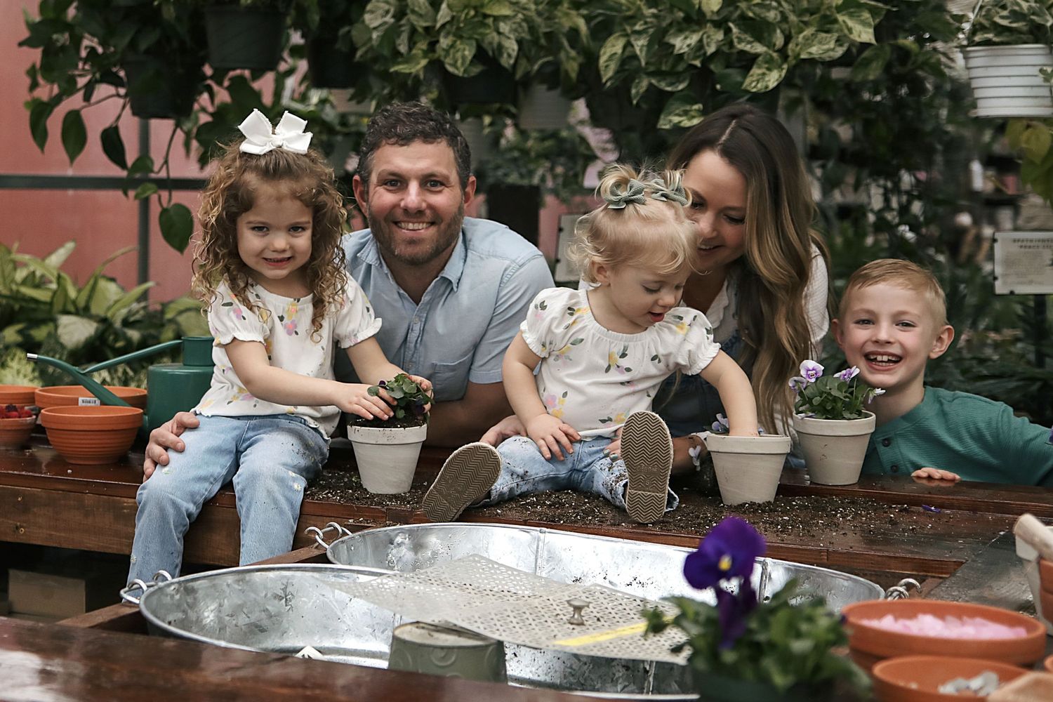 Family gathering around a rustic wooden dining table outdoors with potted plants and seasonal decor.