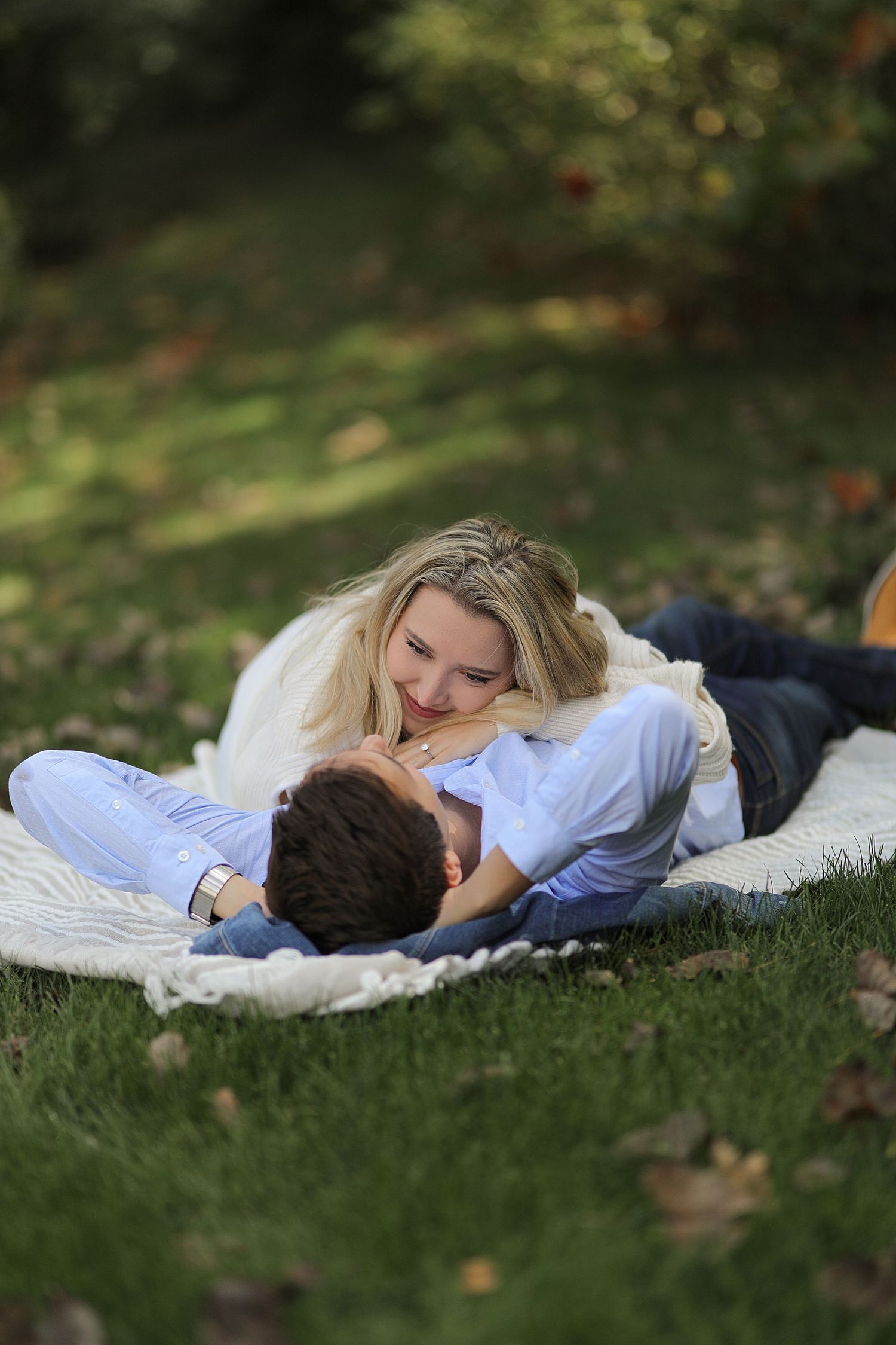 Couple lying together on grass during autumn while sharing an intimate moment in a park setting.