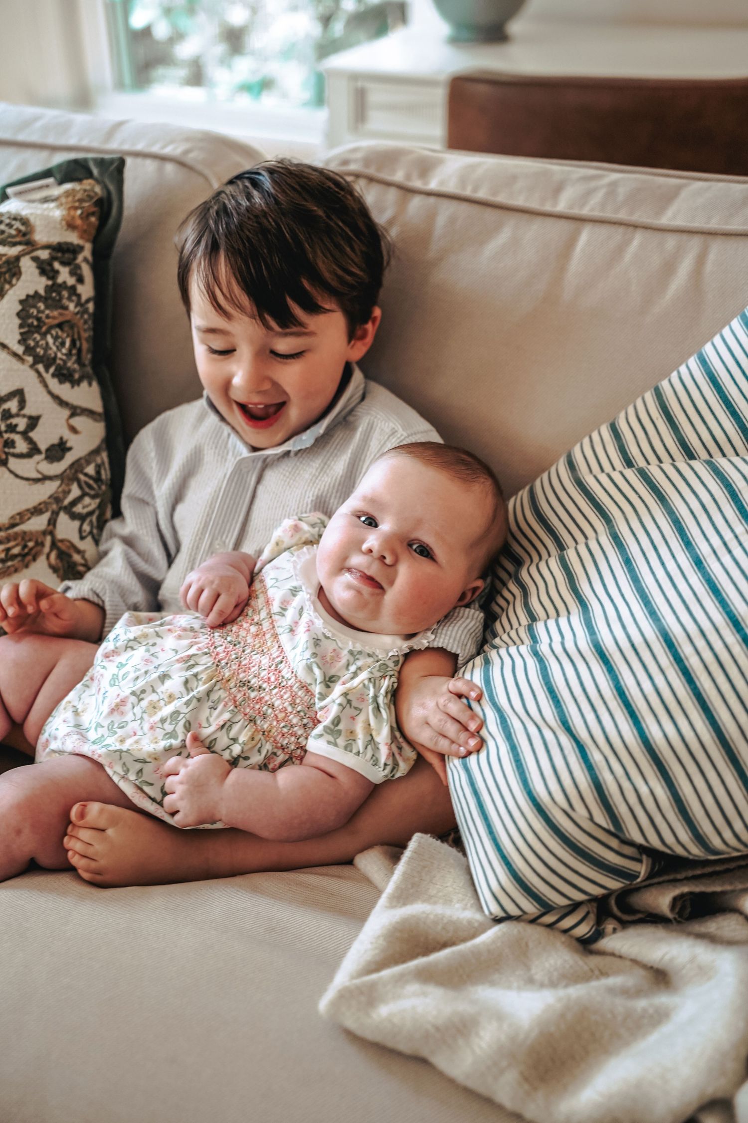 Children cuddling together on a couch with striped pillows and cushions in a tender bonding moment.