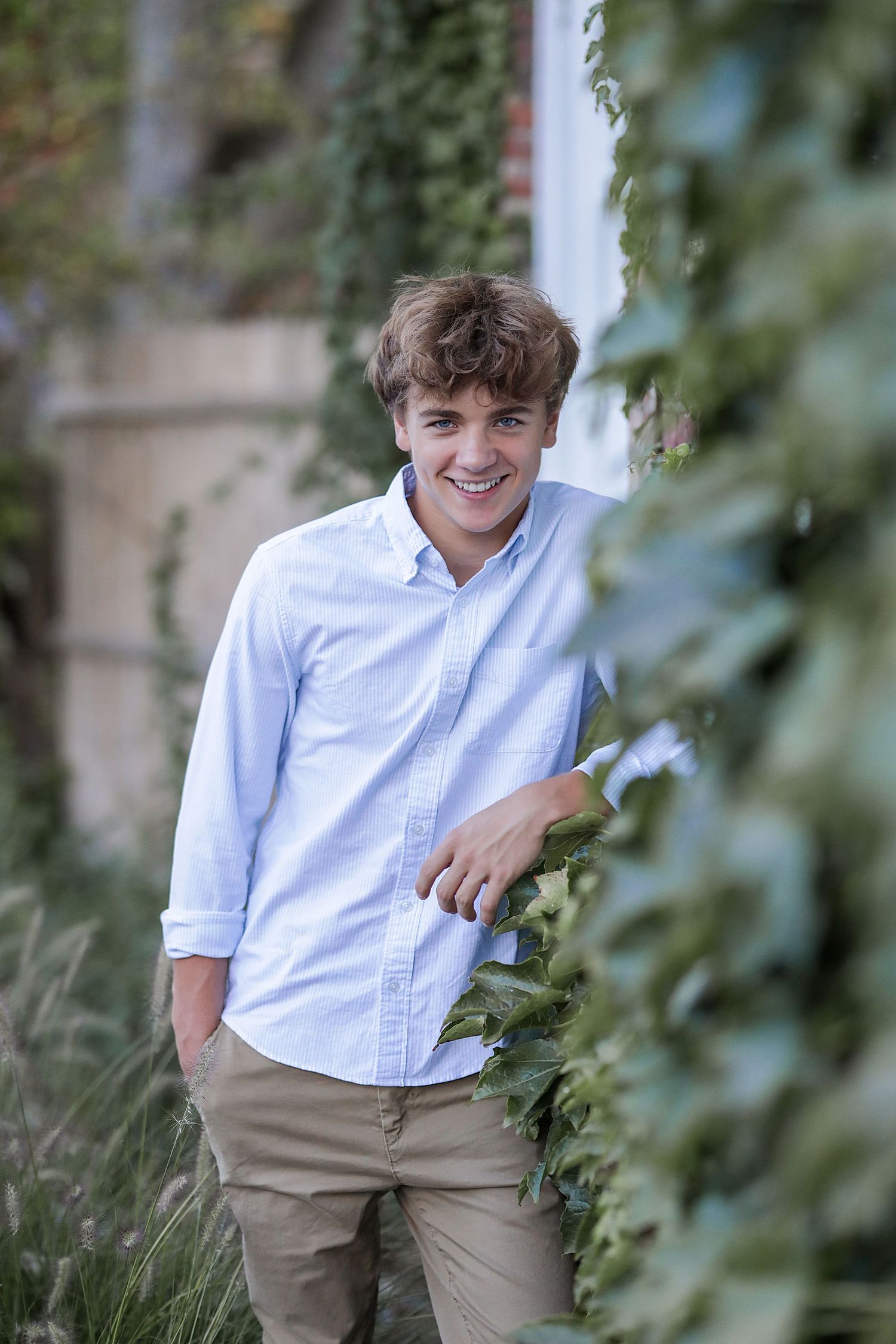 Portrait photo of someone in a light blue button-down shirt and khaki pants standing among greenery outdoors.