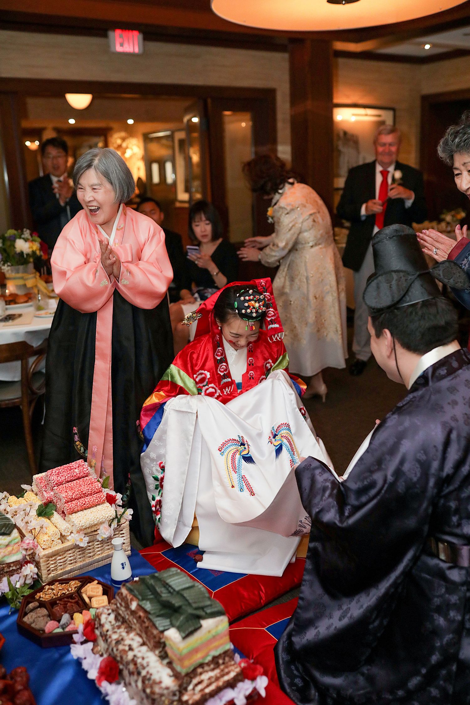 People gathered at an event with red and white decorations and traditional dress viewing items displayed on tables.