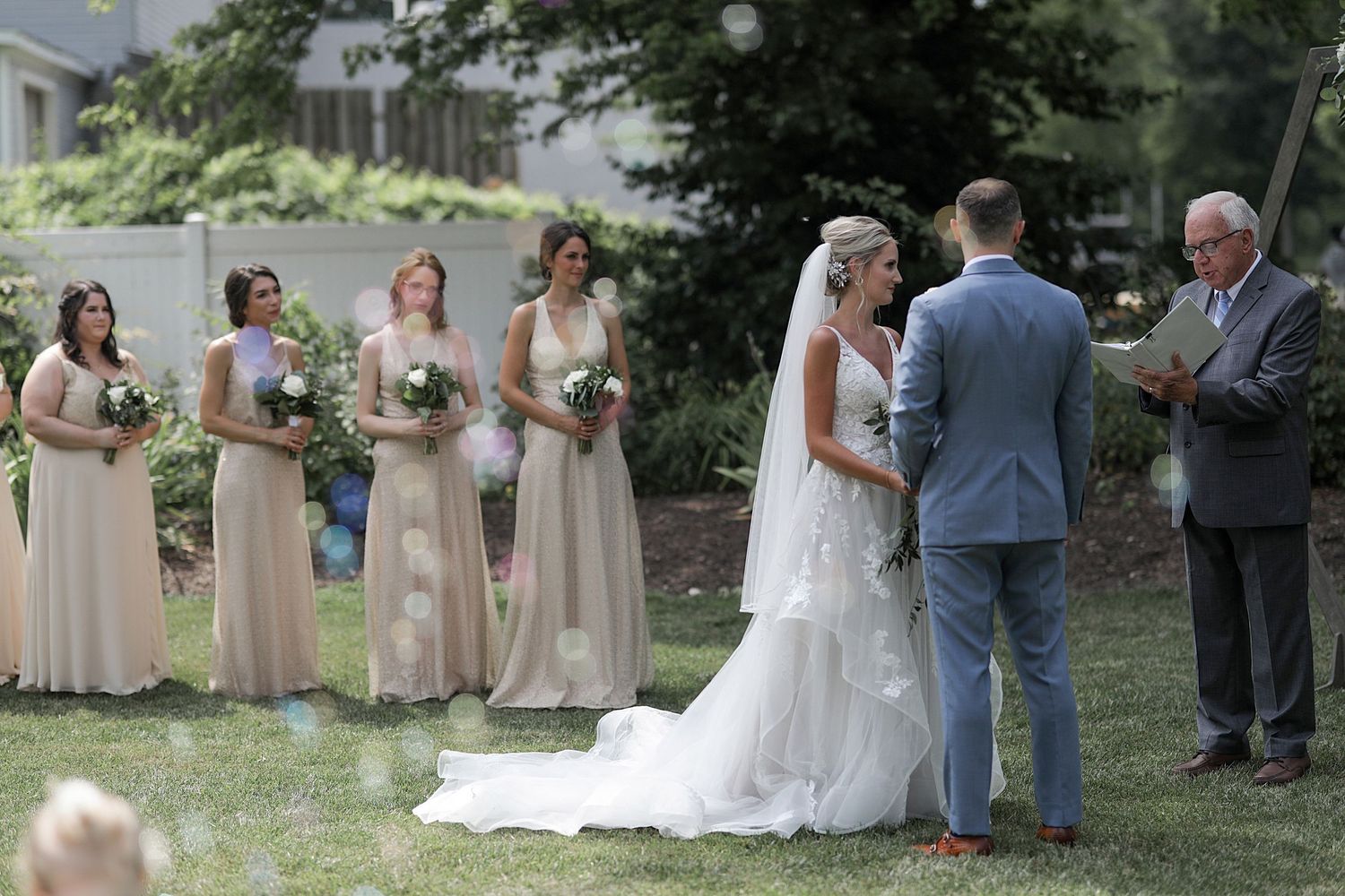 Outdoor wedding ceremony with bridesmaids in beige dresses watching the exchange of vows.