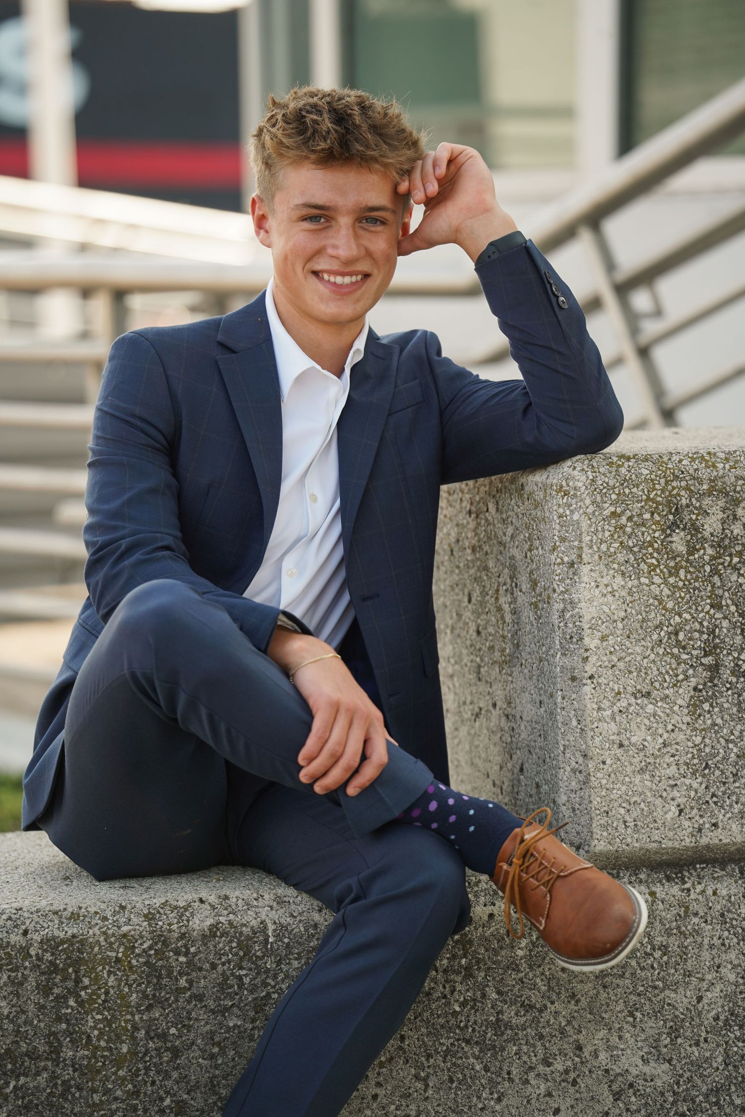 Senior portraits Strongsville, Ohio. A casual portrait of a person in a navy suit sitting on concrete steps outdoors.