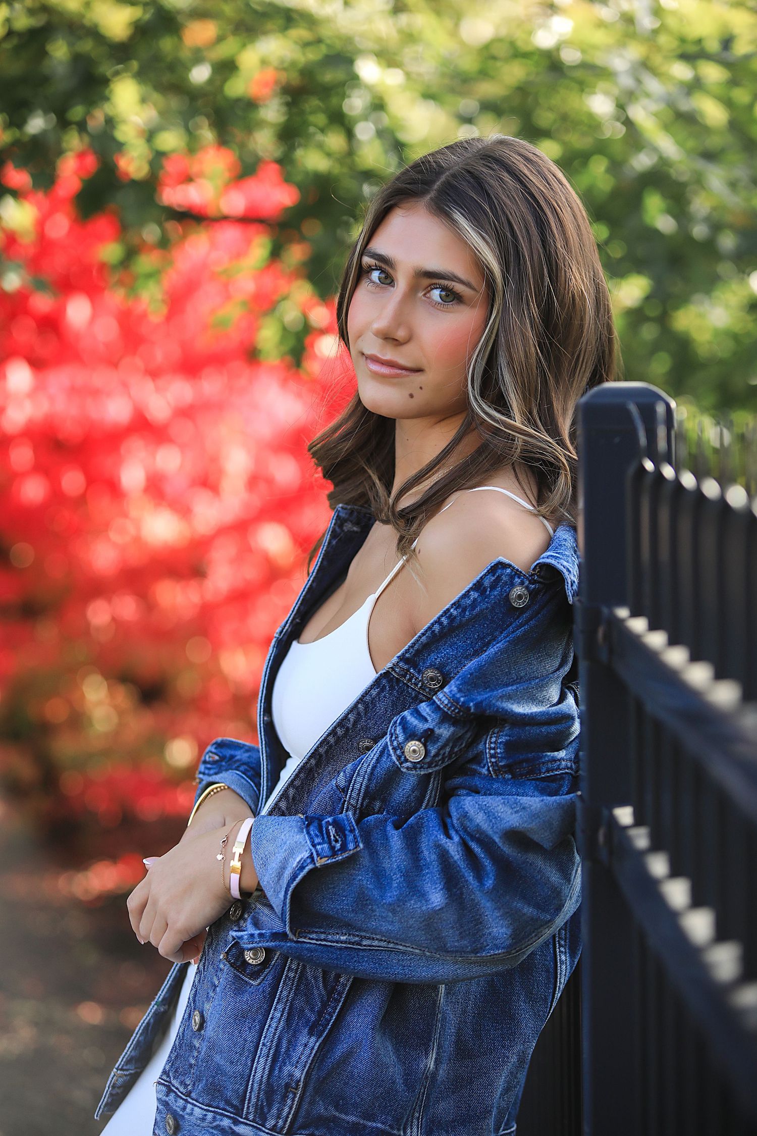A person in a denim jacket poses outdoors against a background of autumn foliage and black railings in a portrait series.