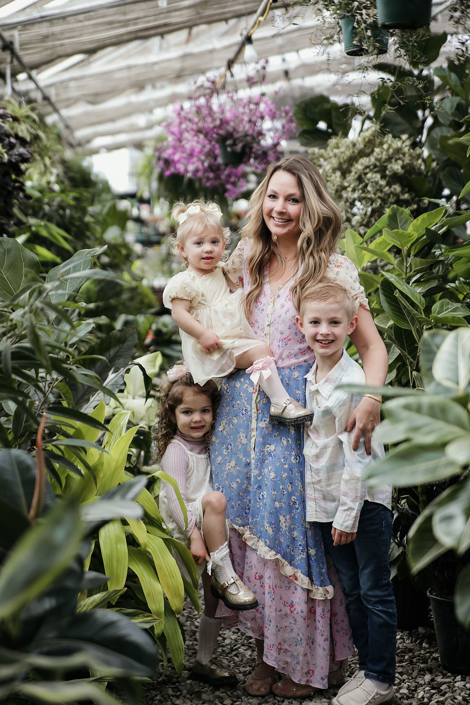 A group of people posing together in a greenhouse filled with lush plants and pink flowers.