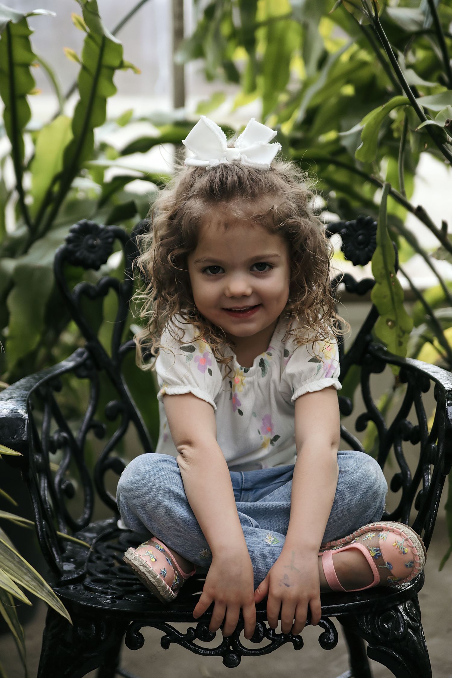 A sequence of photos shows a young child sitting on an ornate black metal bench among green foliage in a garden setting.
