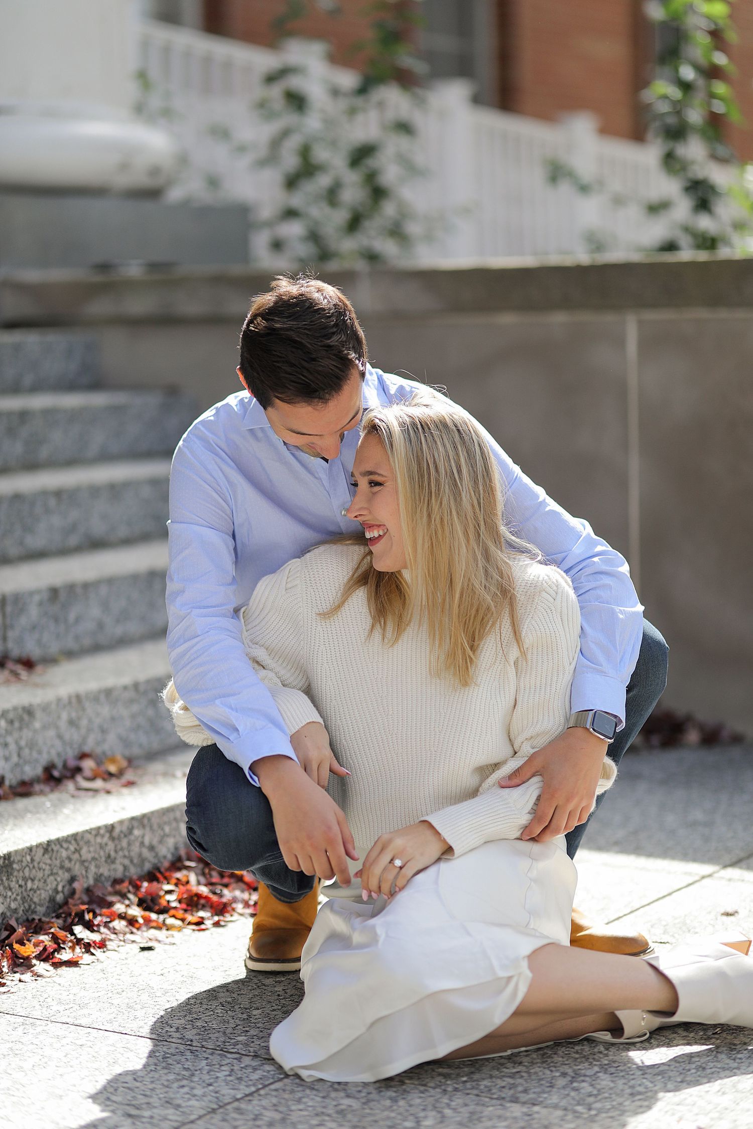 A couple sits together on stone steps outdoors in fall sharing a romantic moment.
