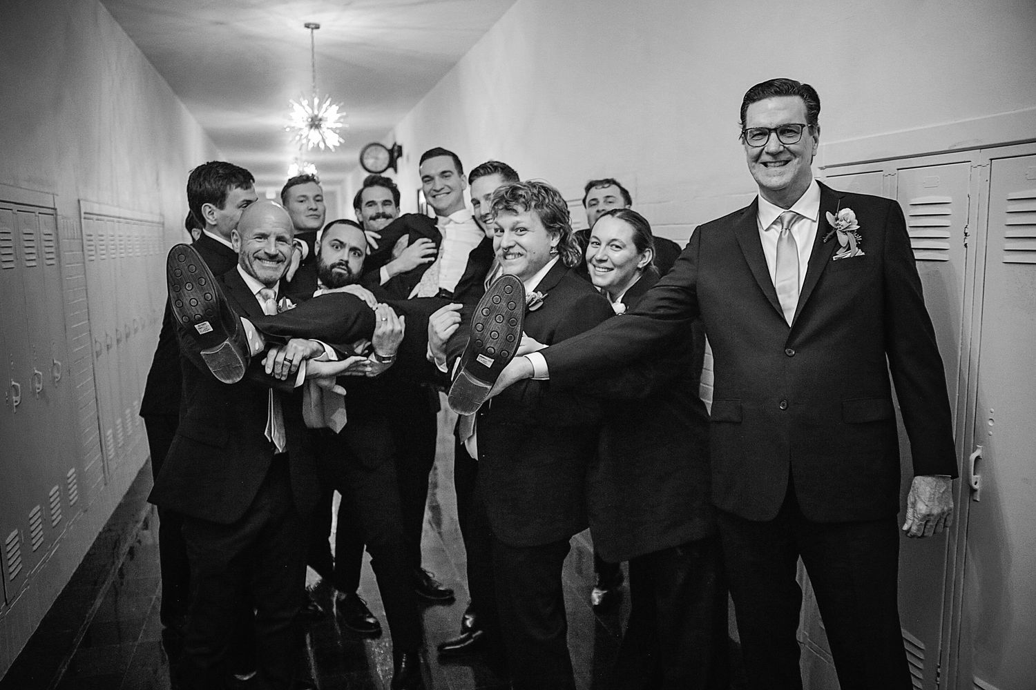 Wedding party members pose playfully in a hallway with lockers creating a fun candid moment.