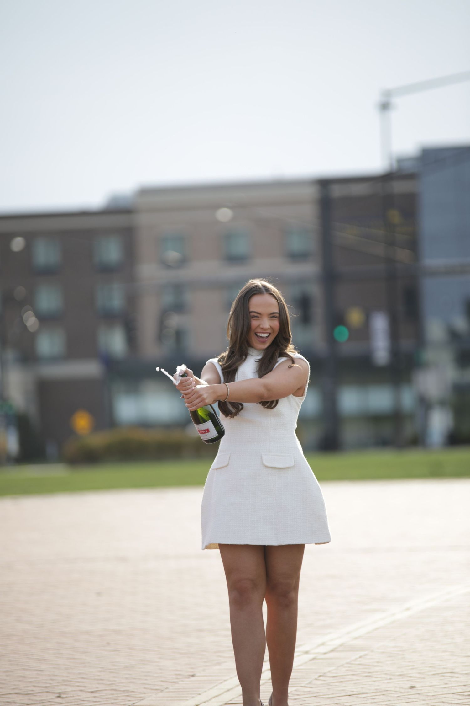 A person wearing a white dress stands outdoors in a parking lot on a sunny day.