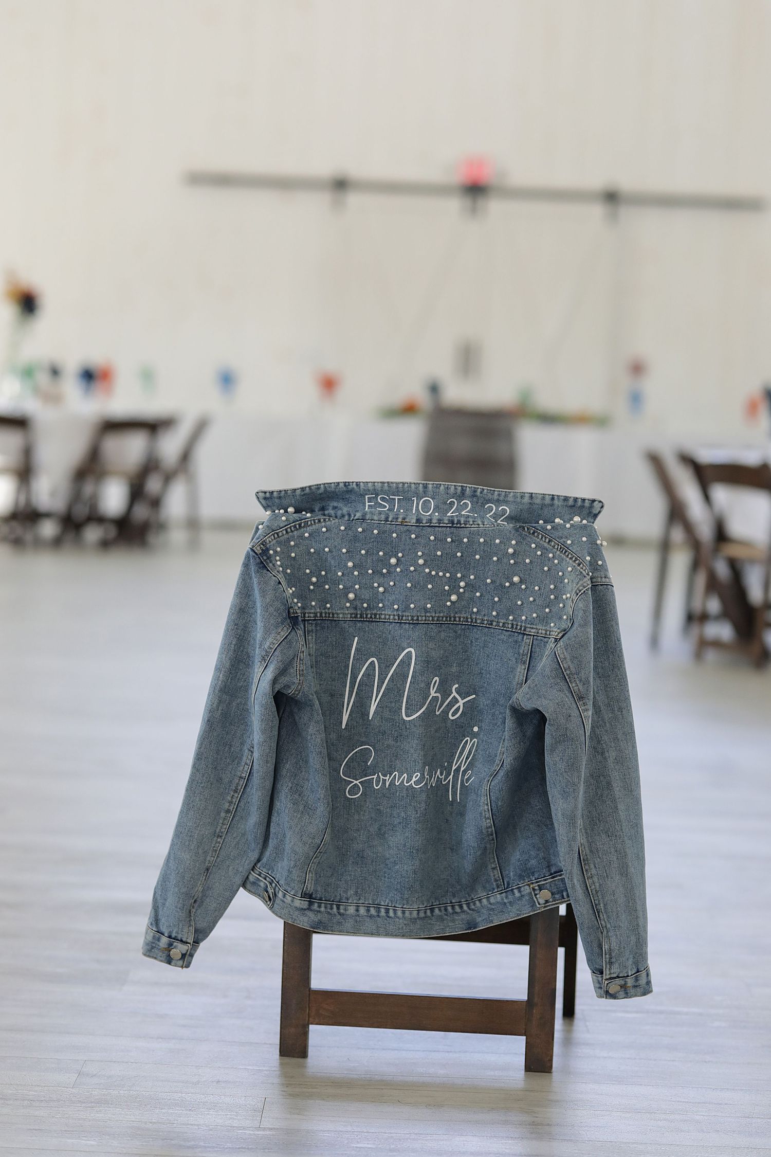A customized denim jacket with 'Mrs' written on it draped over a wooden chair in an empty venue.